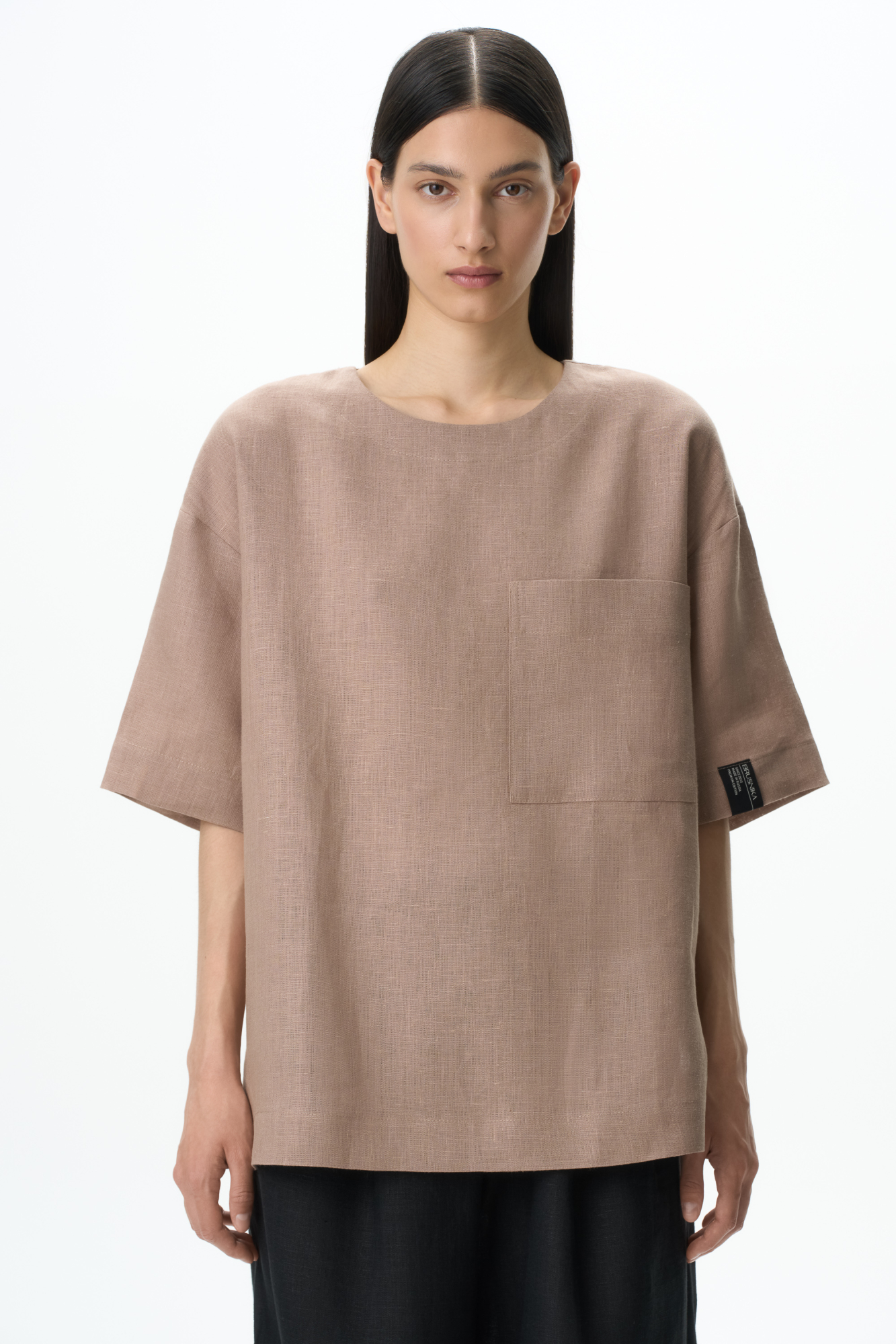 Широкая футболка из 100% льна. Модель прямого кроя, со спущенной линией плеча, круглым вырезом горловины и асимметричным низом с разрезами по бокам. Изделие декорировано накладным карманом на груди и брендированным ярлыком на рукаве. Застежка на пуговицу сзади.