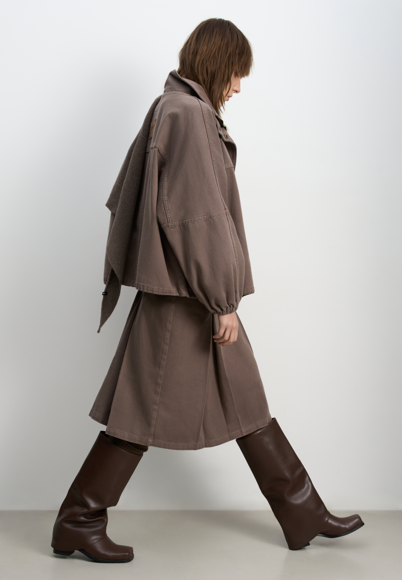 Джинсовая юбка из 100% хлопка длины миди. Модель прямого кроя, с крупными встречными складками, двойным поясом со шлевками для ремня, тонким ремешком и застежкой на молнию сбоку. 