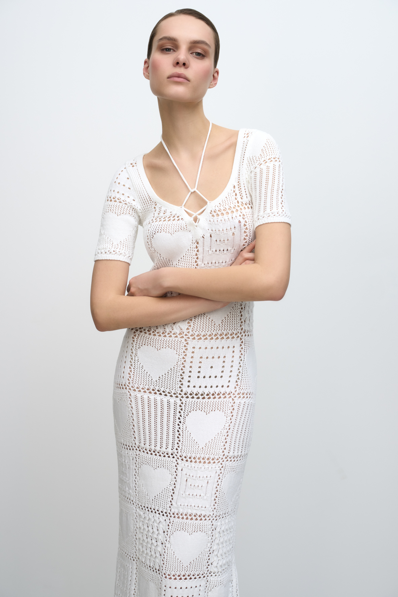 Трикотажное ажурное платье длины миди, выполненное в стиле печворк. Модель приталенного силуэта, с коротким рукавом и кулиской, фиксируемой на шее.