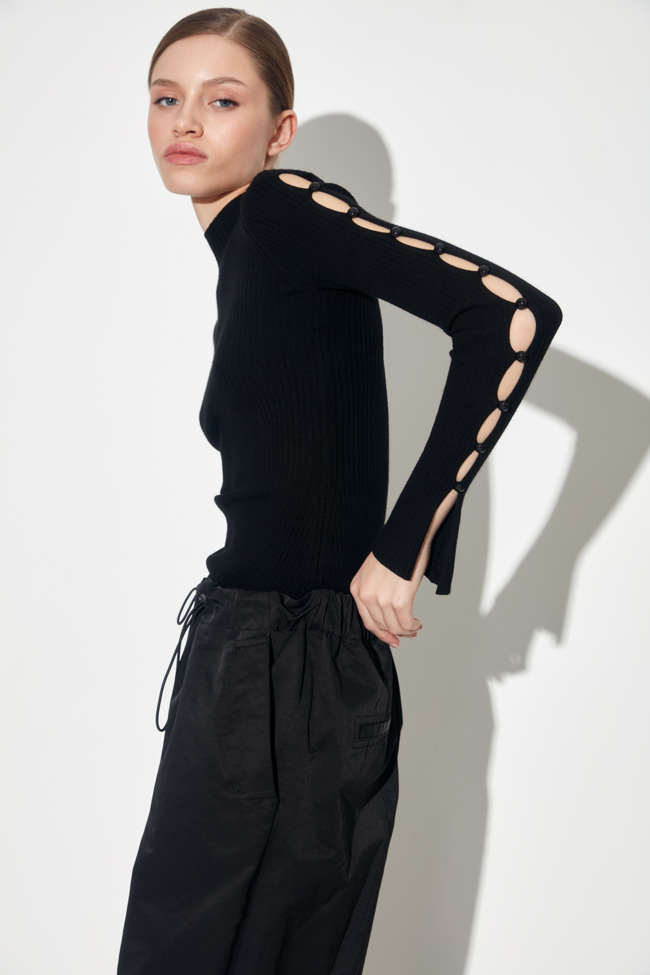 Трикотажный топ из вискозы. Модель приталенного силуэта, разрезами по бокам, с длинными рукавами на пуговицах, невысоким воротником-стойкой и декоративными сбавками на груди.