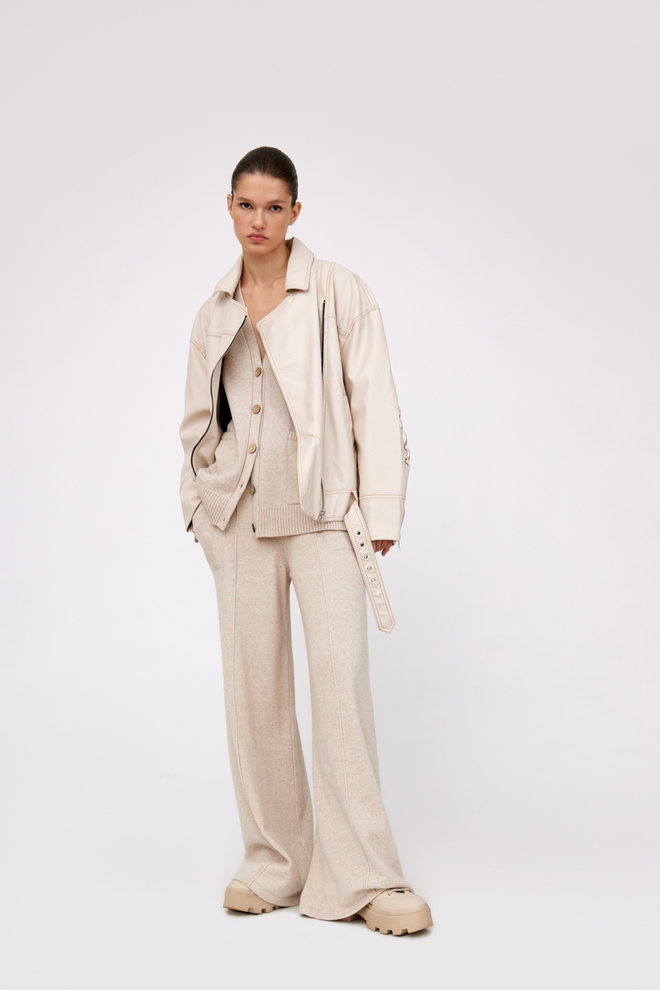 Куртка свободного силуэта из экокожи на подкладке с отложным воротником, боковыми карманами и широким поясом с пряжкой. Длинные рукава декорированы шнуровкой. Асимметричная застежка на молнию.