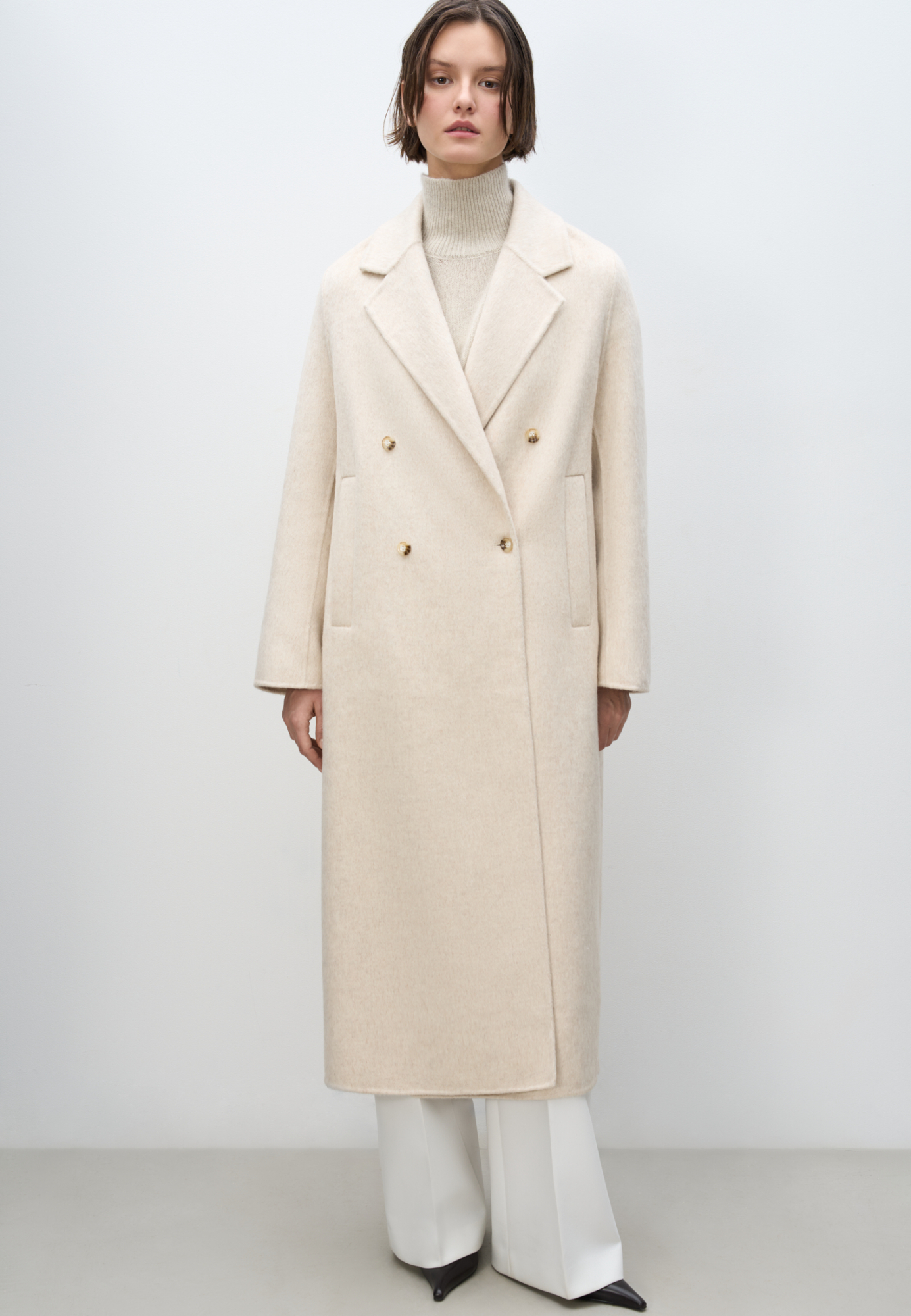 Двубортное шерстяное пальто свободного силуэта с английским воротником, боковыми карманами и застежкой на пуговицы.