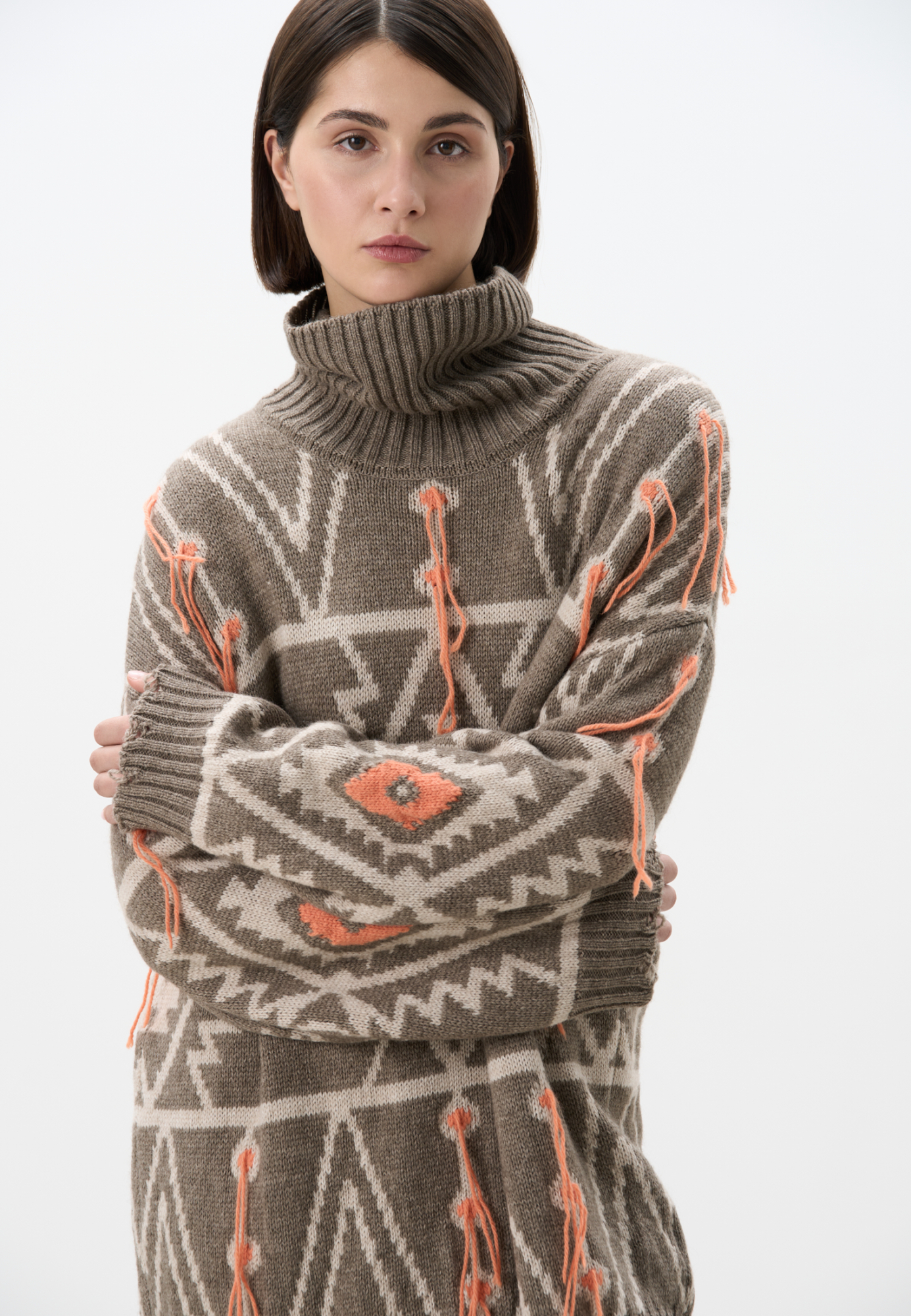 Трикотажный джемпер из шерсти альпака с геометрическим жаккардовым орнаментом. Модель свободного силуэта с высоким воротом и со спущенной линией плеча. Края изделия выполнены в рубчик. Изделие декорировано локаничной бахромой.