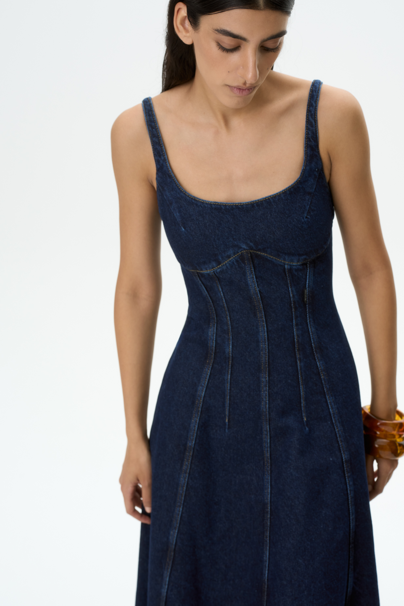 Джинсовое платье длины миди из 100% хлопка. Модель приталенного силуэта, с вытачками на талии, акцентным лифом, на тонких бретельках, вертикальными рельефными швами и необработанным низом.