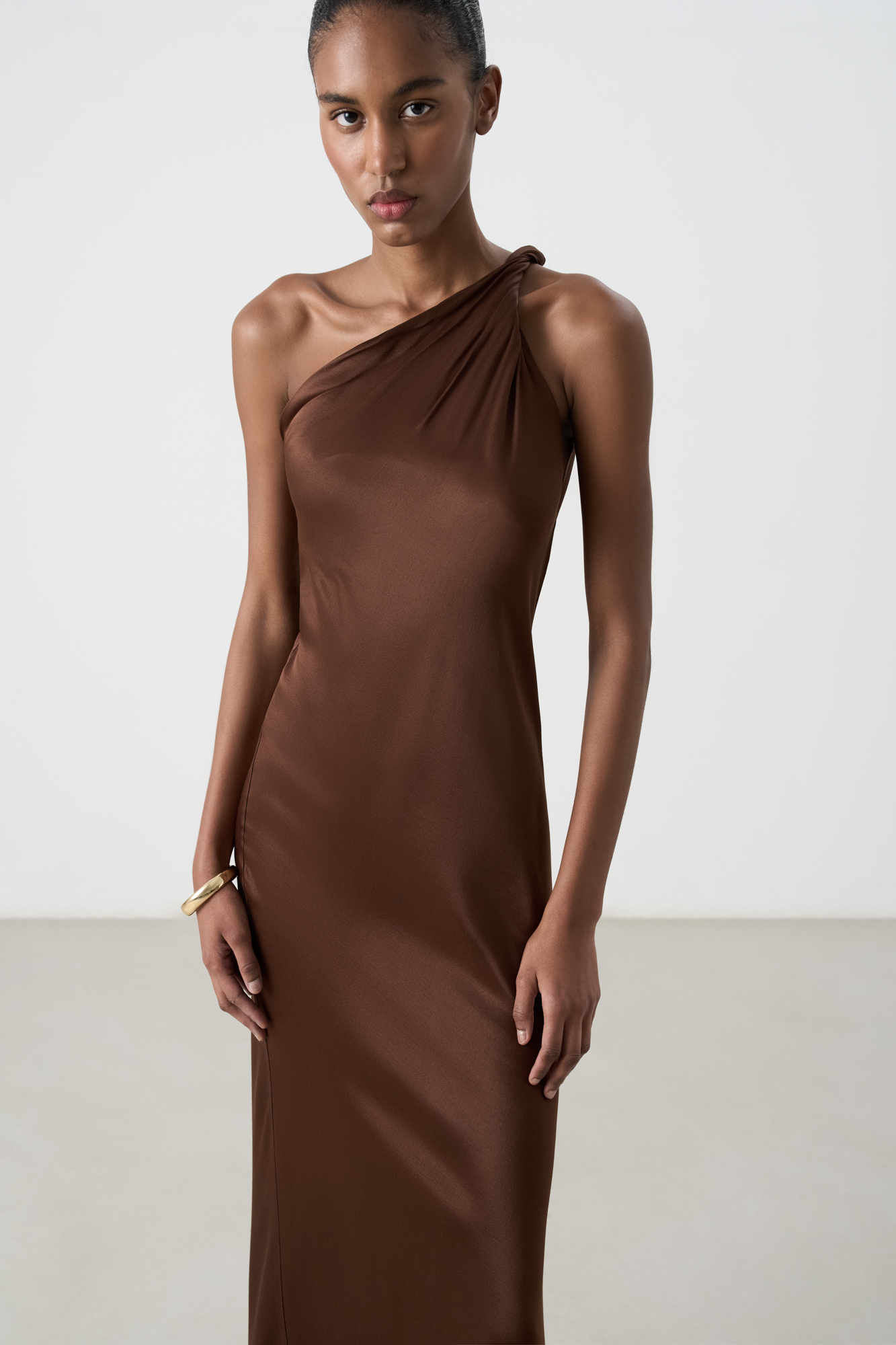 Платье длины макси из атласной вискозы. Модель приталенного силуэта, без рукавов, с перекрученной лямкой на одно плечо и разрезом сбоку.