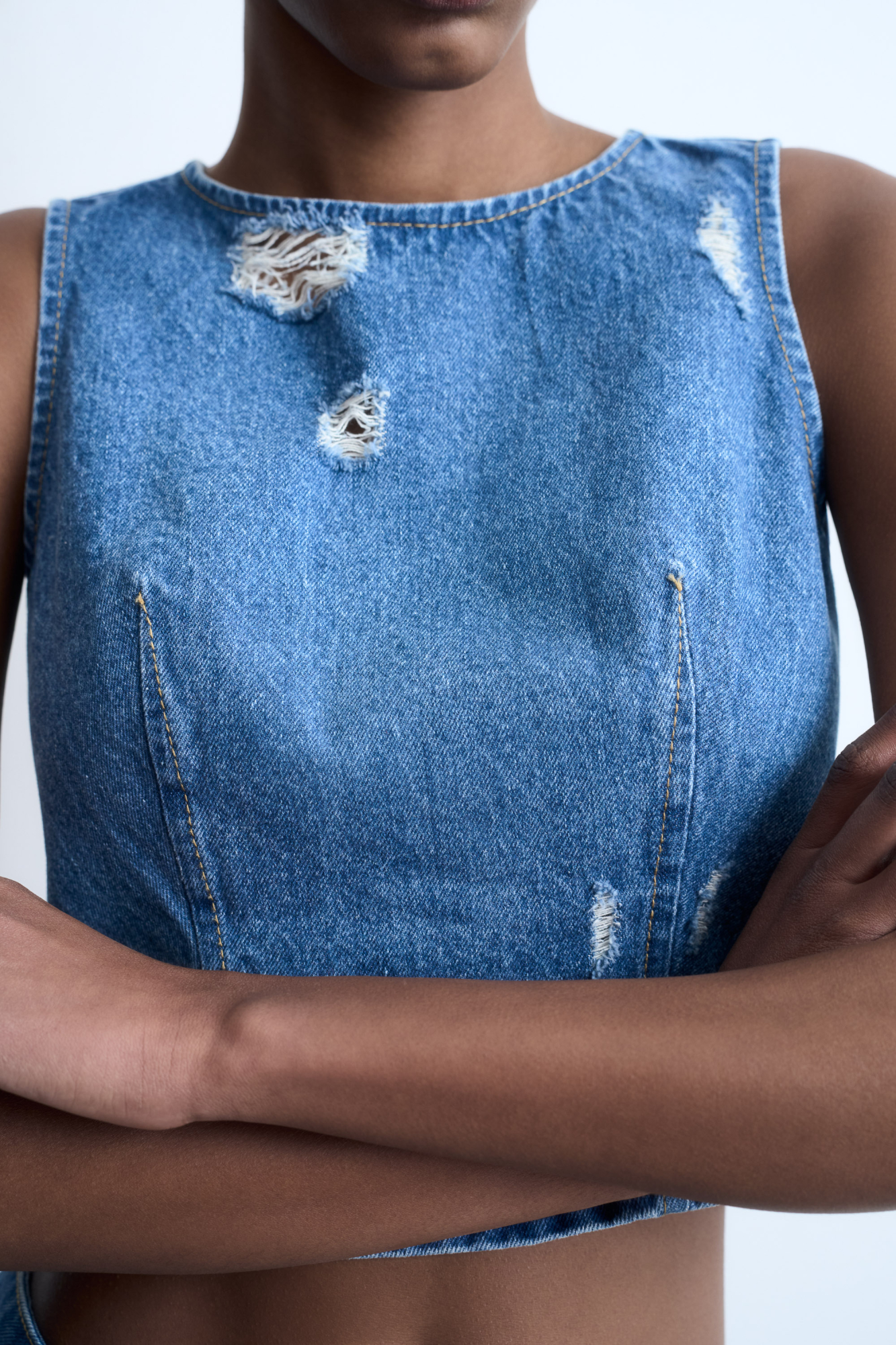 Джинсовый удлиненный топ с разрезами в стиле гранж. Модель приталенного силуэта, без рукавов. Дополнить образ можно юбкой в таком же стиле.