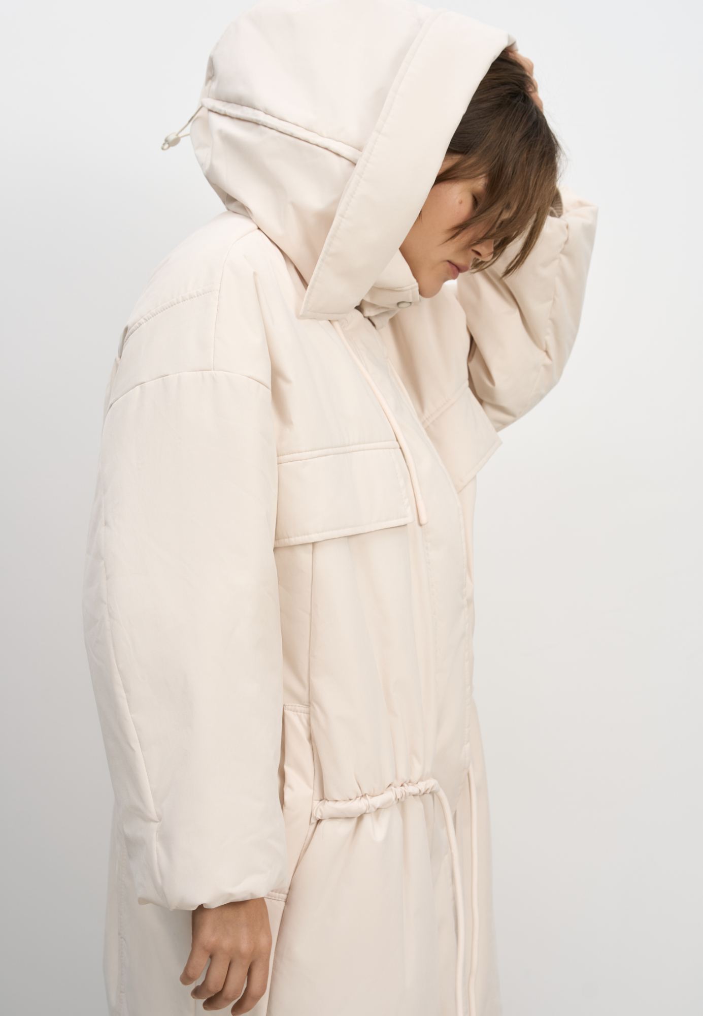 Длинная куртка на синтепоне с капюшоном. Модель свободного силуэта со спущенной линией плеча, накладными и боковыми карманами, регулируемой кулиской на поясе. Изделие на подкладке. Застежка на молнию и магнитные кнопки.