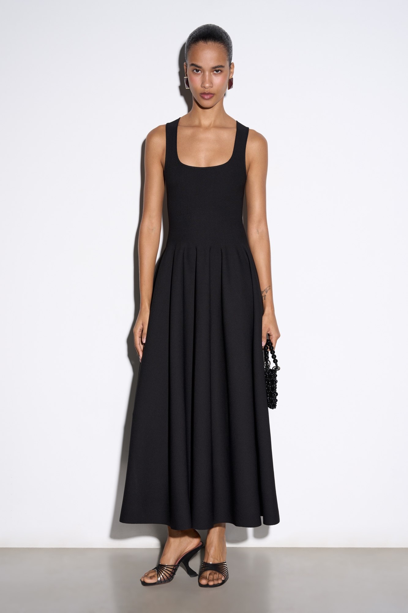 Трикотажное платье длины миди из вискозы. Модель приталенного силуэта с расклешенной юбкой с мягкими складками, без рукавов, на широких бретелях и квадратным вырезом. 