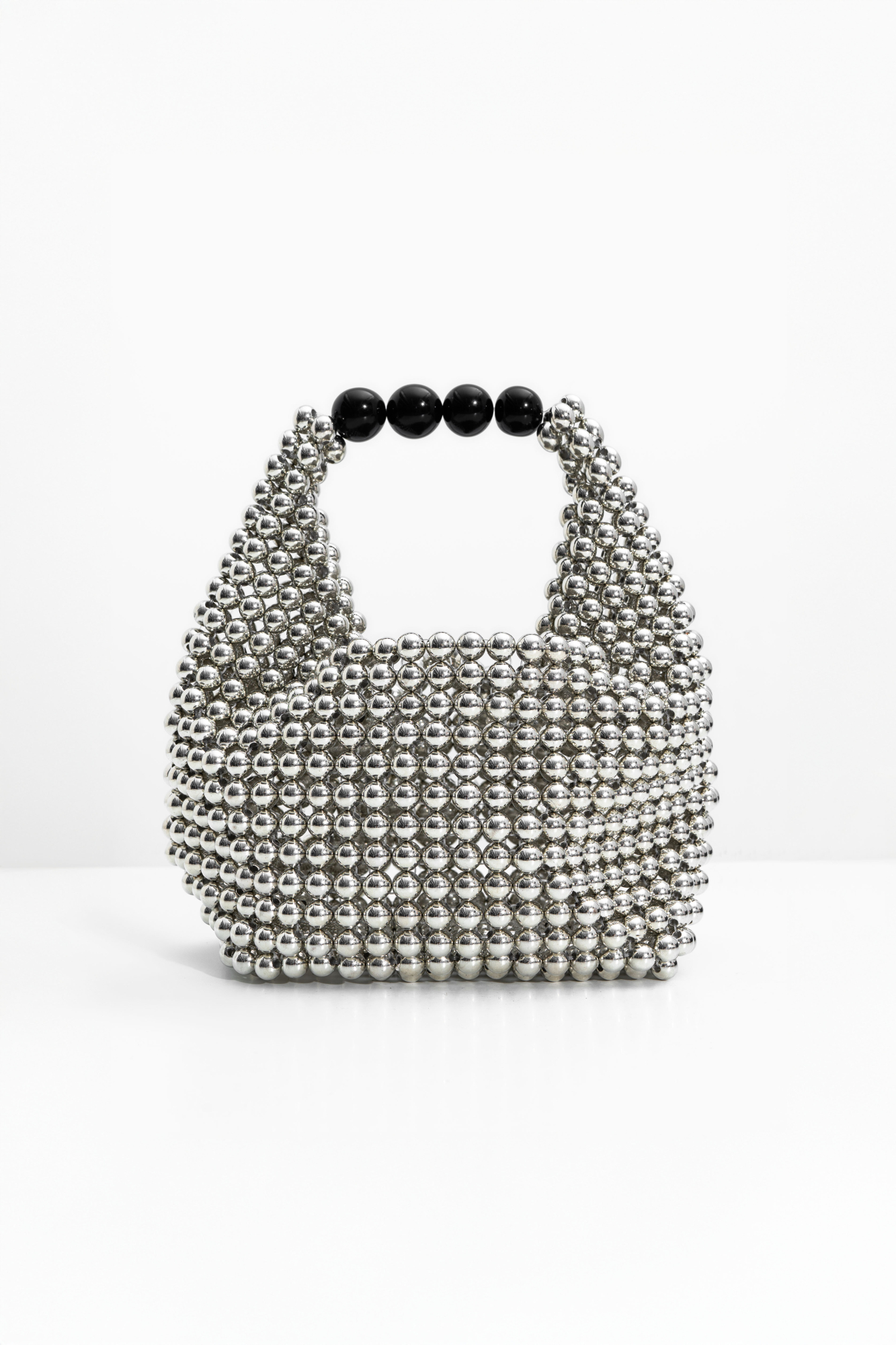 Сумочка, изготовленная путем переплетения серебряных бусин. Модель с одной короткой ручкой и черным бантом в комплекте. Высота изделия составляет 12 см, длина ручки - 13 см.