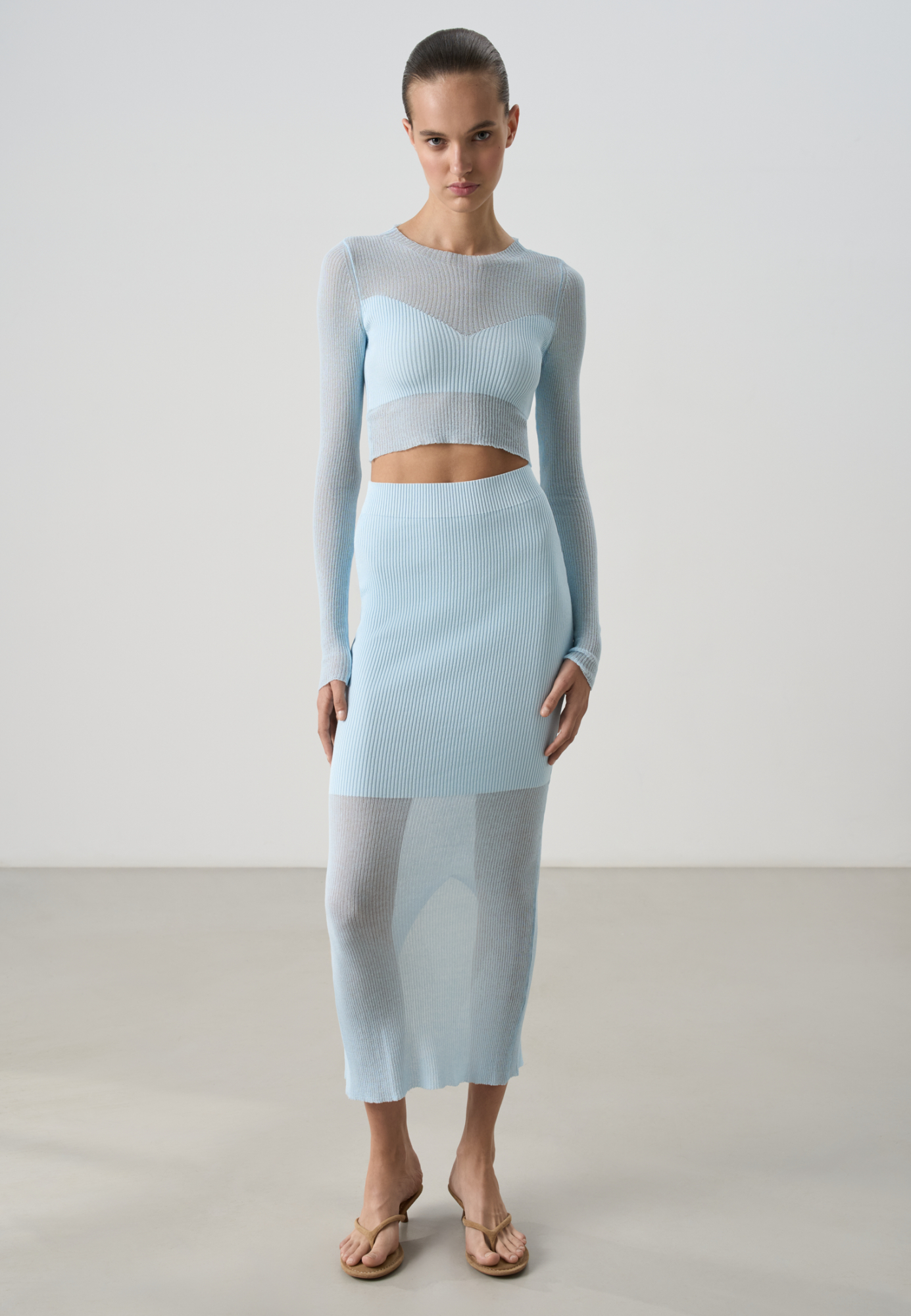 Трикотажная юбка длины миди из тонкого хлопка с добавлением вискозы. Изделие выполнено в комбинированной вязке, сочетая более плотную и полупрозрачную текстуры. Модель приталенного силуэта, с широким эластичным поясом и разрезом сзади.