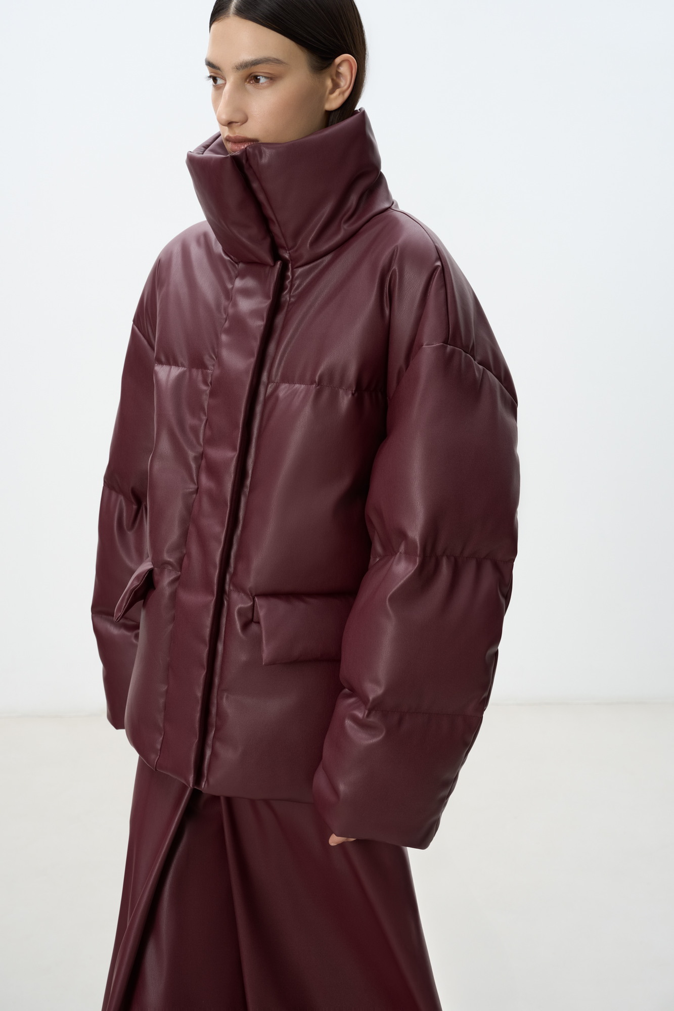 Утепленный пуховик из экокожи. Модель свободного силуэта с боковыми карманами и воротником-стойкой. Застежка на потайную молнию и магнитные пуговицы. На подкладке.