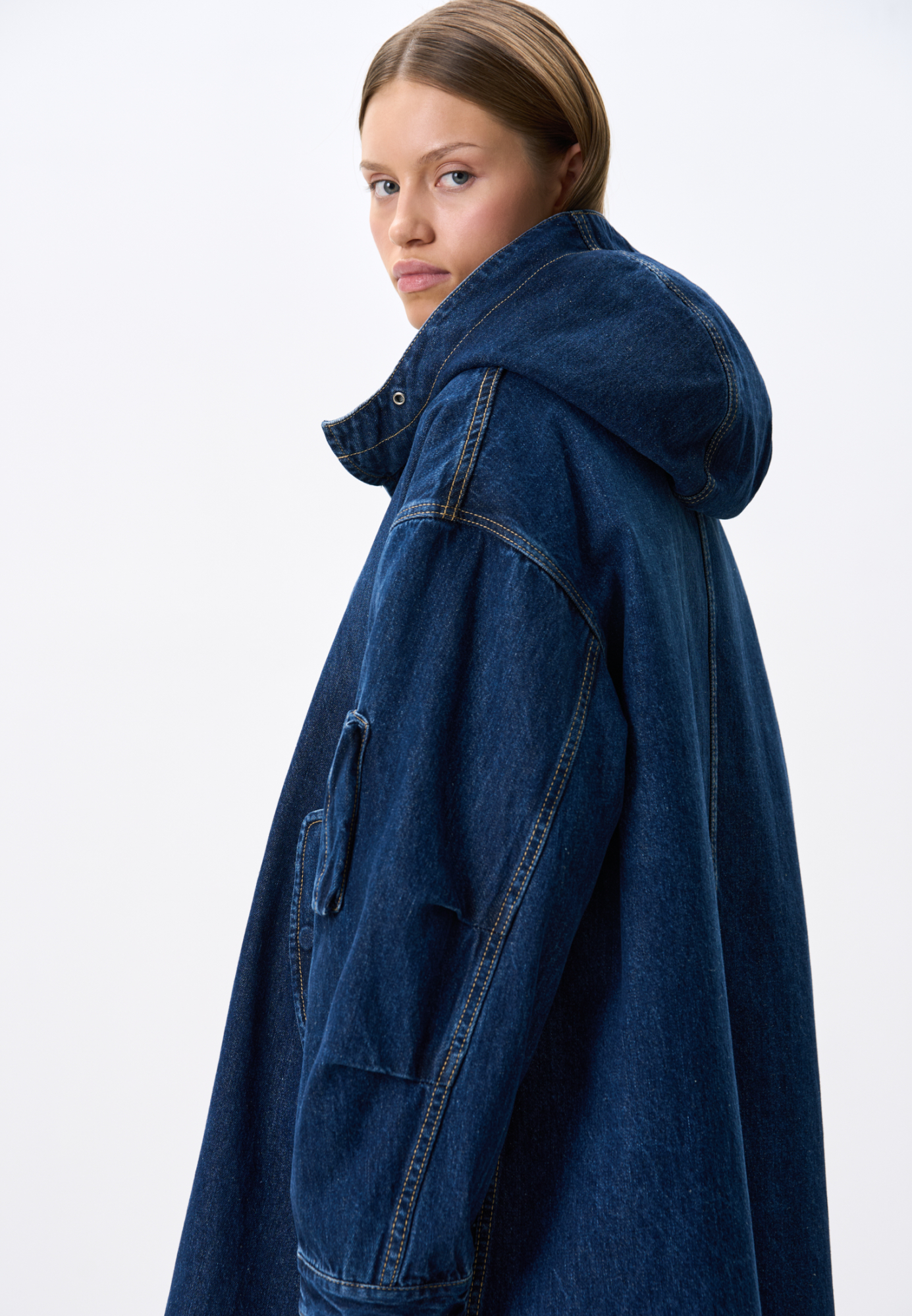 Джинсовая парка из 100% хлопка на стеганой подстежке. Модель свободного кроя, со спущенной линией плеч, глубоким капюшоном, боковыми карманами с клапанами на пуговицах и карманом на рукаве. Застежка на металлические кнопки под планкой. Подстежка отстегивается и может являться отдельным элементом образа. 