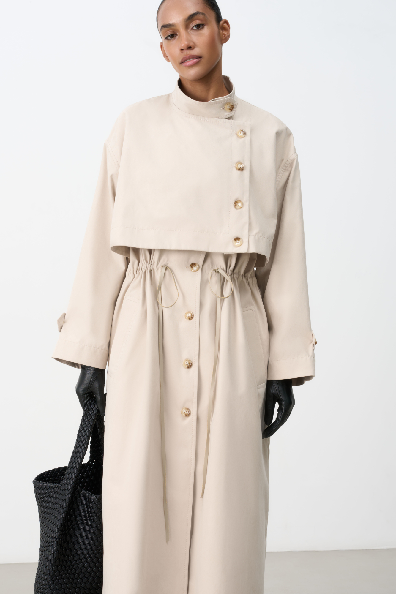 Однобортный тренч с асимметричной отлетной кокеткой. Модель свободного кроя, с воротником-стойкой, патами на манжетах и боковыми карманами. Акцент на талию с помощью регулируемой кулиски. Изделие без подкладки. Застежка на пуговицы.