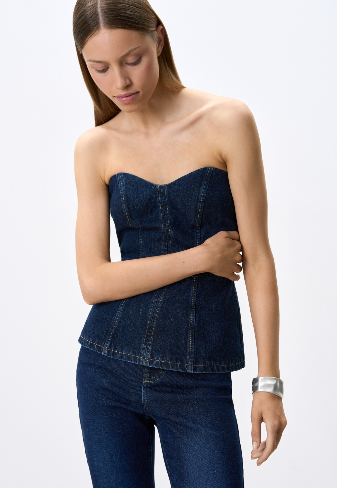 Джинсовый корсет из 100% хлопка. Модель имеет фактурный лиф и расклешеннный книзу силуэт. Изделие  декорировано строчкой контрастного цвета. Застежка на молнию сзади.