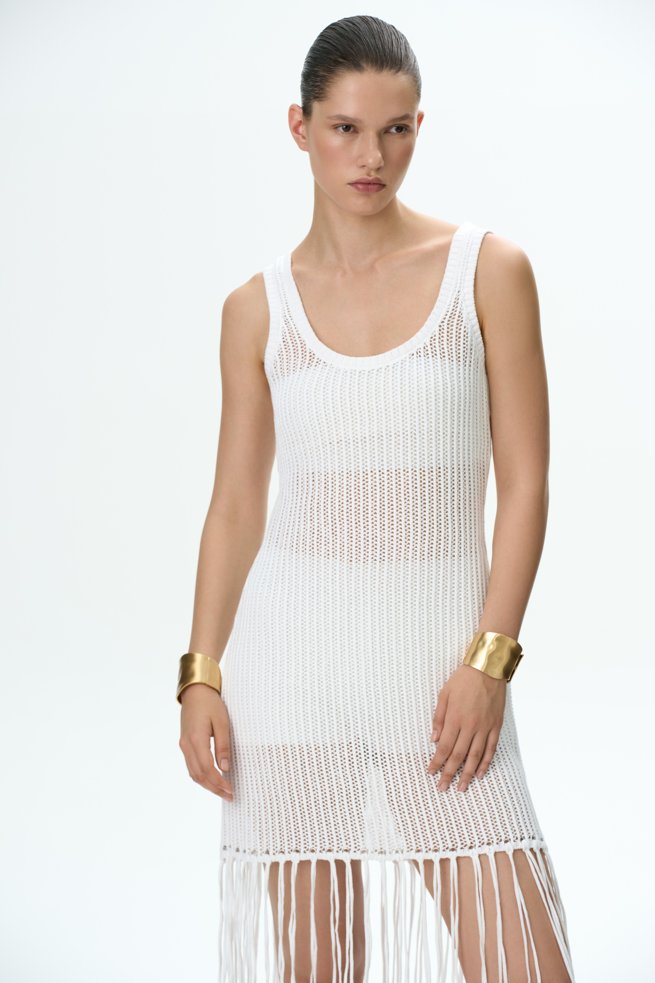 Трикотажный ажурный сарафан из 100% хлопка. Модель свободного кроя, без рукавов, на широких бретельках и U-образным вырезом. Изделие декорировано длинной бахромой.