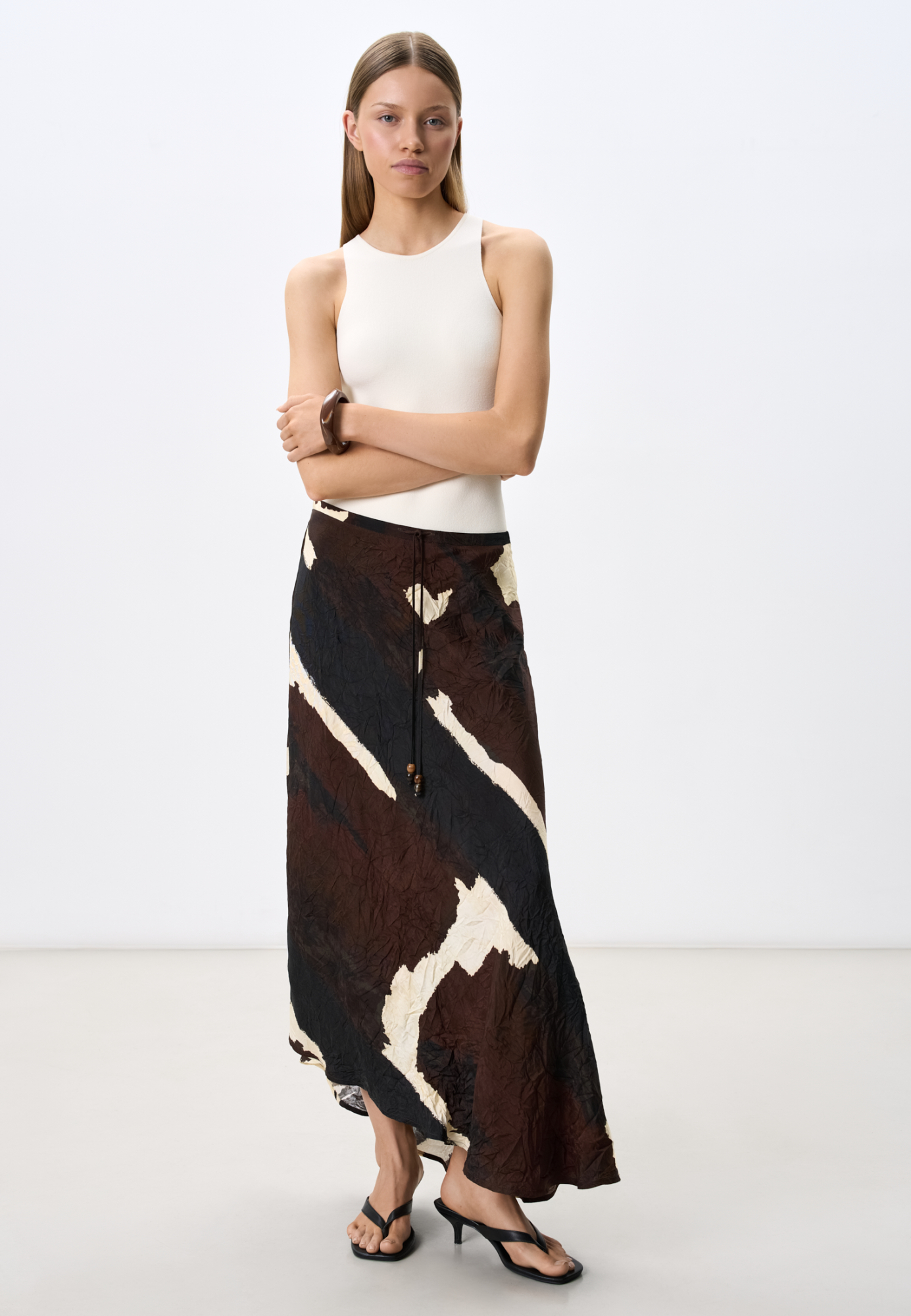 Трикотажная юбка из тонкой вискозы свободного силуэта. Модель А-силуэта с асимметричным низом, узким шнурком, декорированным бусинами и застежкой на молнию сбоку.