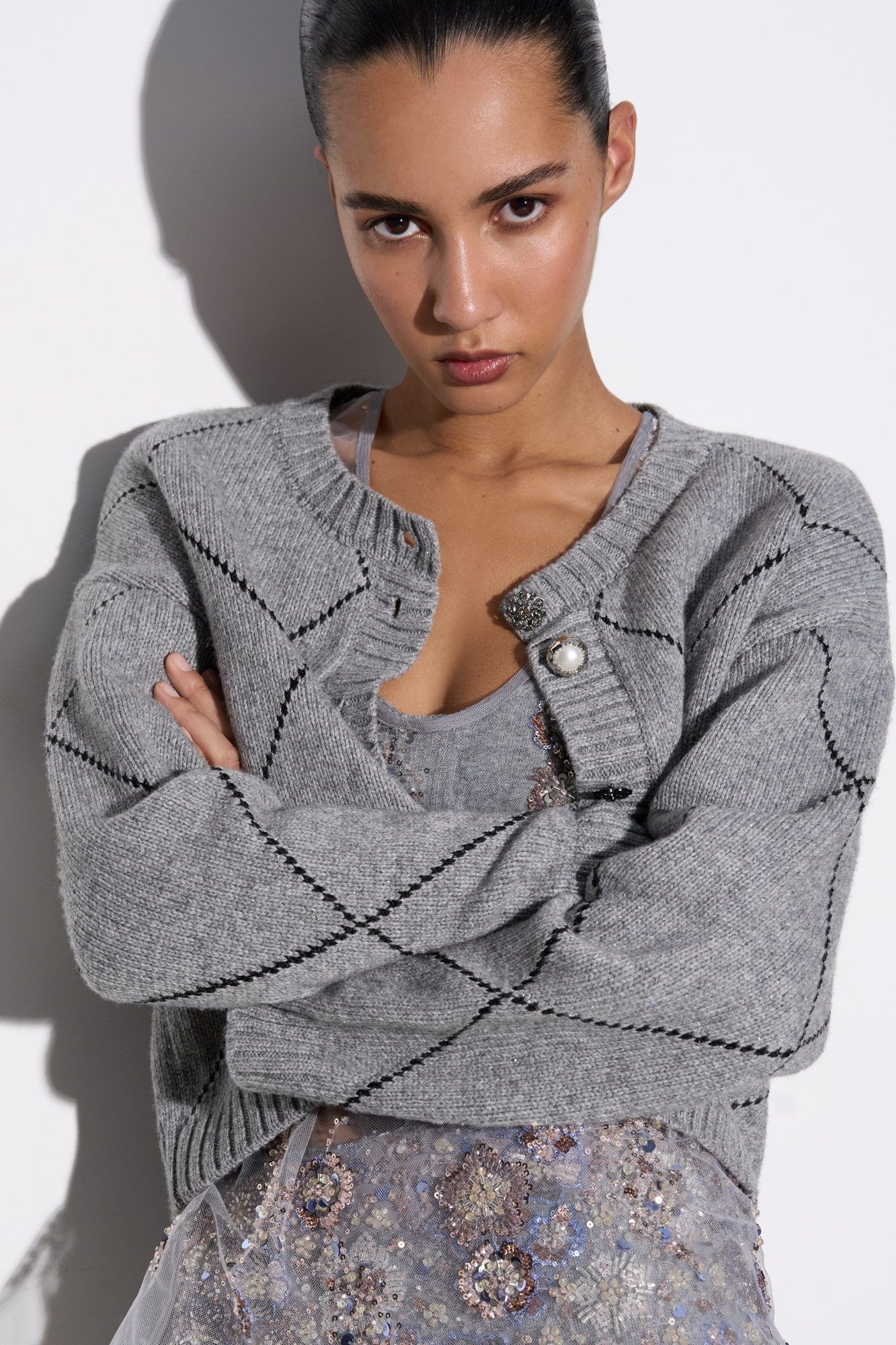 Трикотажный кардиган с узором аргайл из шерсти яка с добавлением люрекса. Модель свободного силуэта со спущенной линией плеч, круглым вырезом горловины и застежкой на крупные пуговицы. Края изделия выполнены в рубчик.