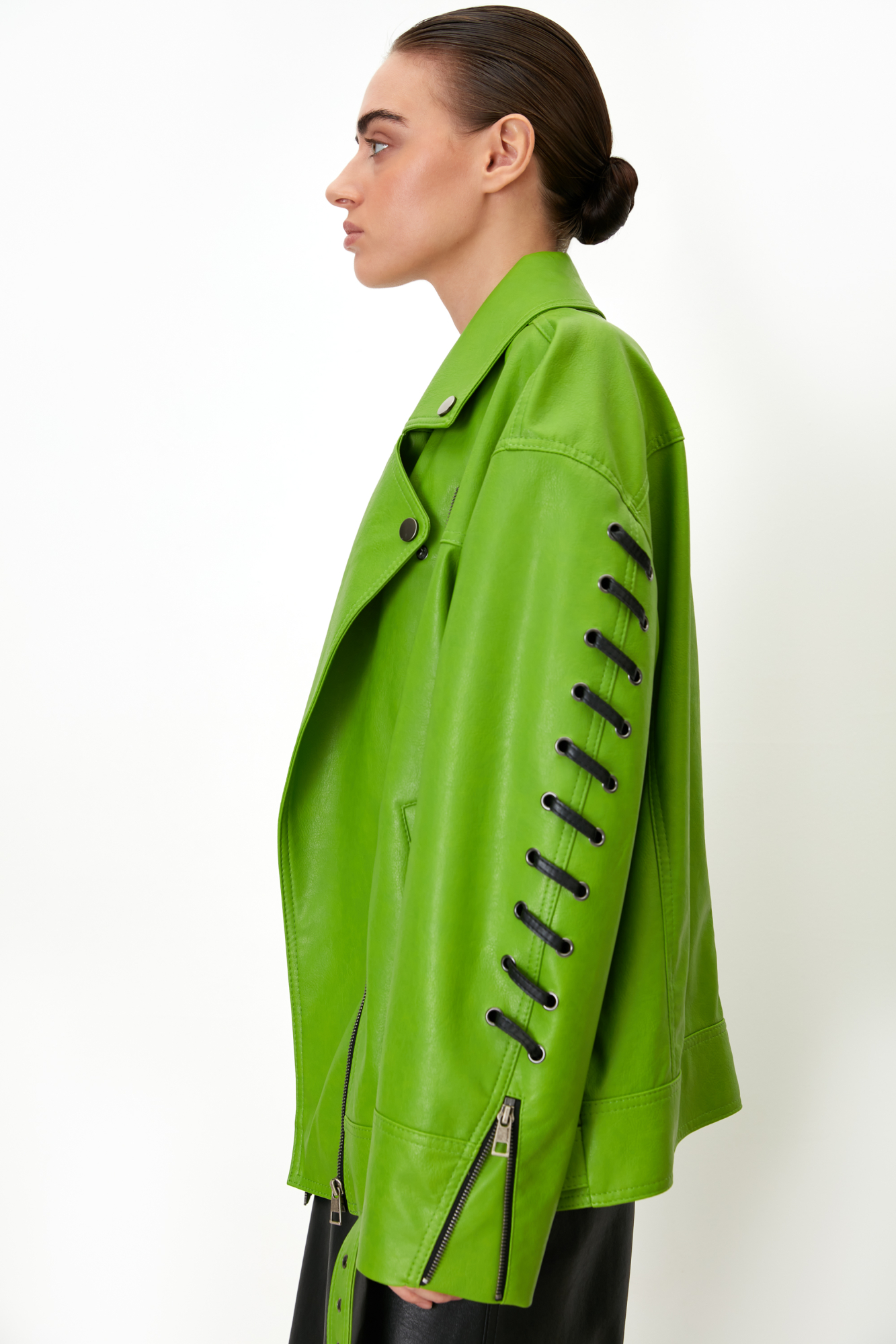 Куртка свободного силуэта из экокожи на подкладке с отложным воротником, боковыми карманами и широким поясом с пряжкой. Длинные рукава декорированы шнуровкой. Асимметричная застежка на молнию.