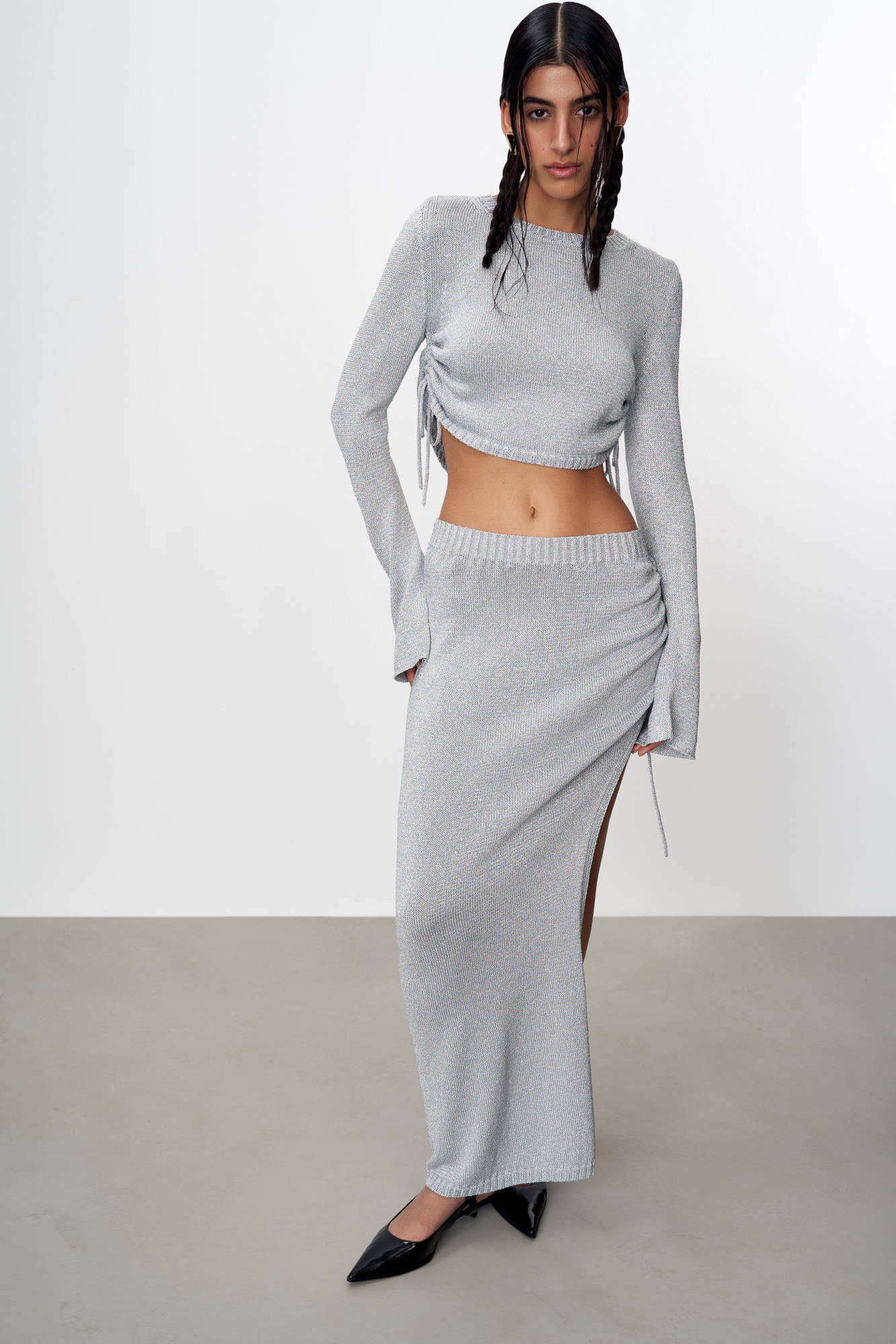 Трикотажная юбка длины макси из вискозы с люрексом. Модель облегающего силуэта, с эластичным поясом в рубчик и разрезом от бедра с кулиской. Дополнить образ можно топом в таком же стиле.