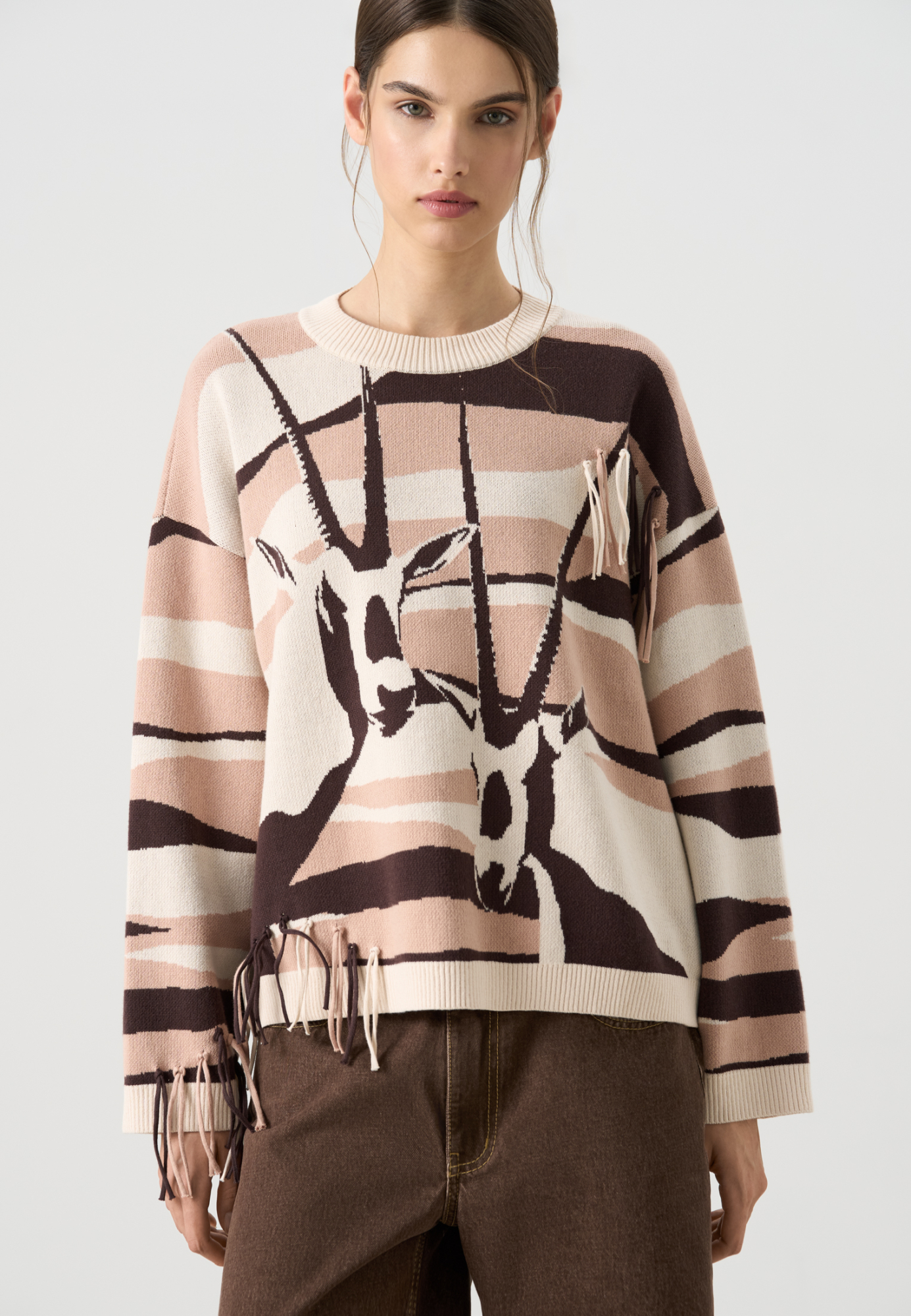 Трикотажный джемпер из 100% хлопка с жаккардовым изображением антилопы орикса. Модель свободного силуэта, с длинными рукавами, спущенной линией плеч и круглым вырезом горловины. Изделие декорировано бахромой в тон джемпера. Края выполнены в рубчик.