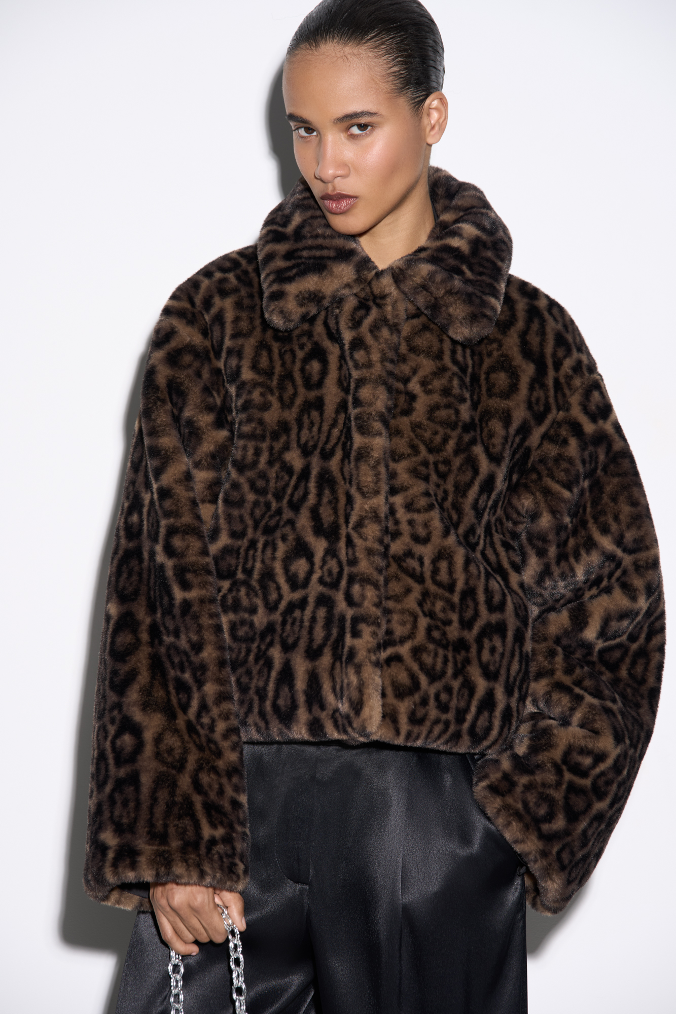 Короткая шуба из экомеха с анималистичным принтом, имитирующим окрас леопарда. Модель прямого кроя с отложным воротником и карманами. Застежка на потайные кнопки под планкой. Низ изделия выполнен на кулиске. 