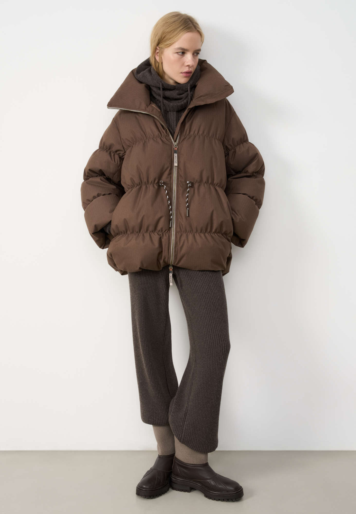 Стеганый объемный пуховик. Модель свободного силуэта, с воротником-стойкой, кулиской на талии и логотипом бренда на спине. Застежка на молнию. 