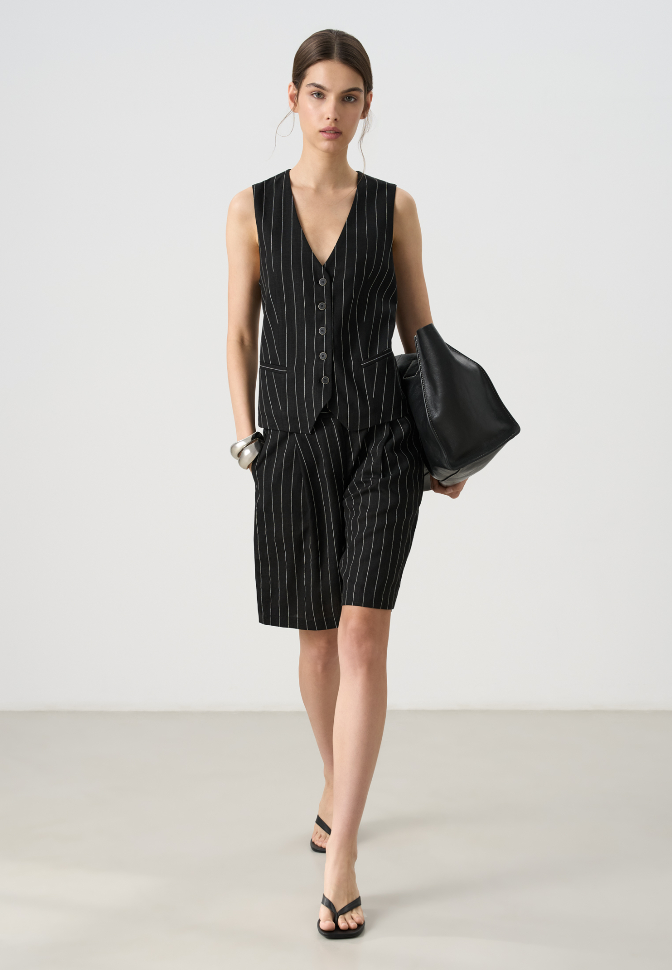 Льняной костюм в полоску из жилета и шорт. Классический жилет прямого кроя, с V-образным вырезом и застежкой на пуговицы. Короткие шорты с боковыми карманами и шлевками на поясе для ремня.Застежка на молнию и пуговицу.