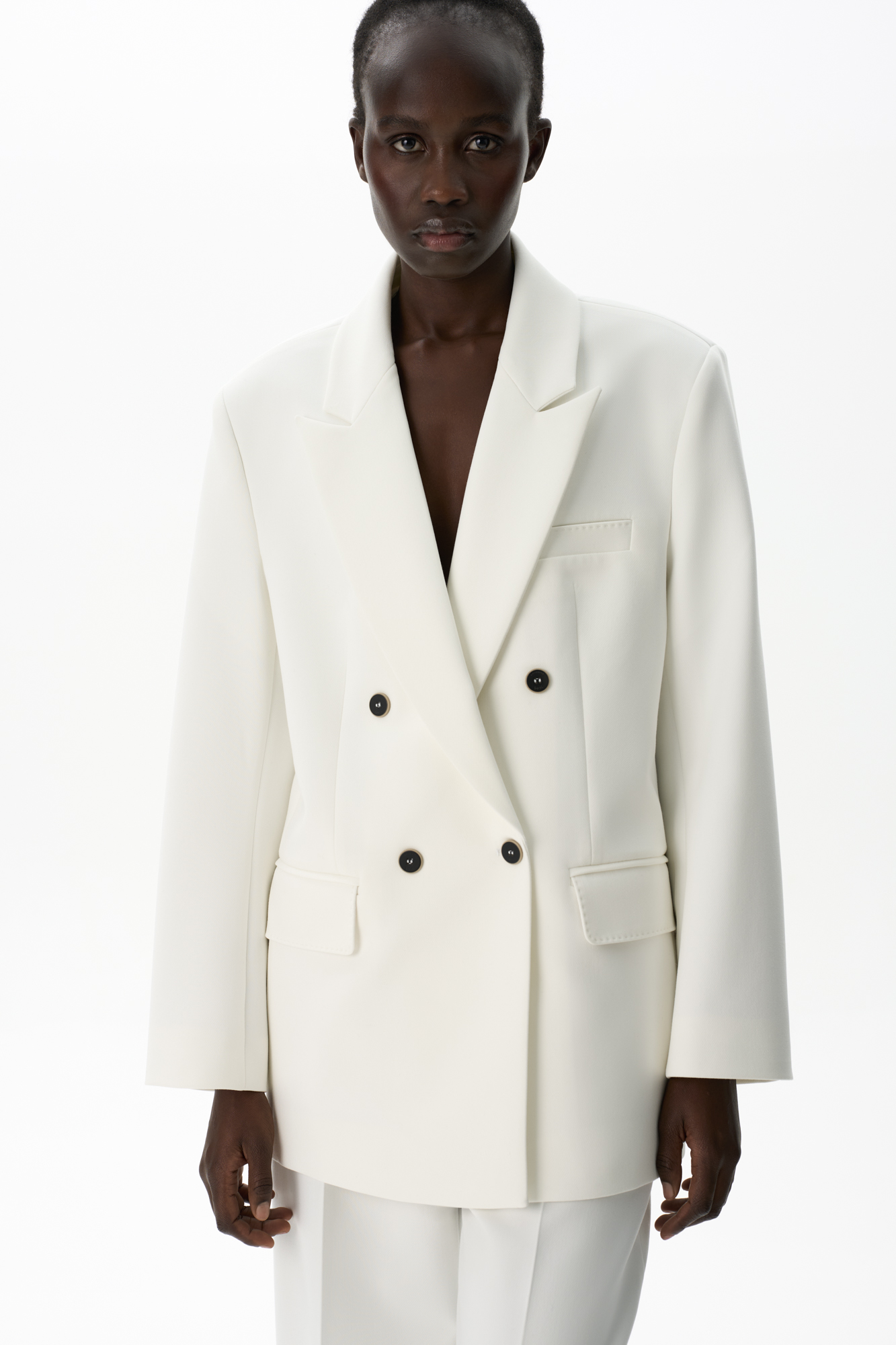 Двубортный жакет с отстрочкой. Модель прямого кроя с лацканами. Два прорезных кармана с клапанами и нагрудный карман. Манжеты декорированы пуговицами. 