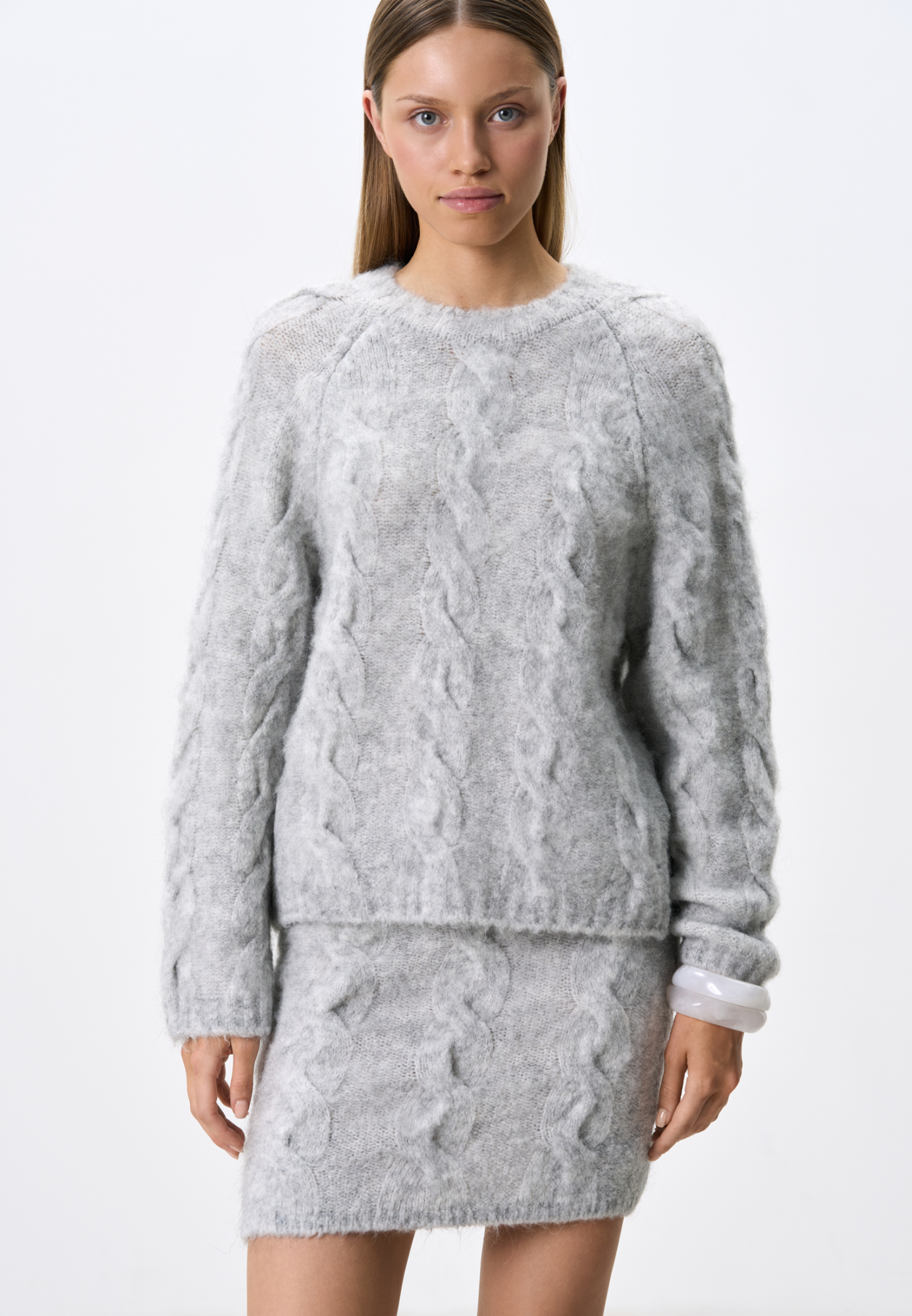 Трикотажный джемпер из шерсти и мохера. Модель свободного силуэта со спущенной линией плеч, объемными рукавами и круглым вырезом горловины. Изделие декорировано фактурной вязкой в виде кос. Края выполнены в рубчик.