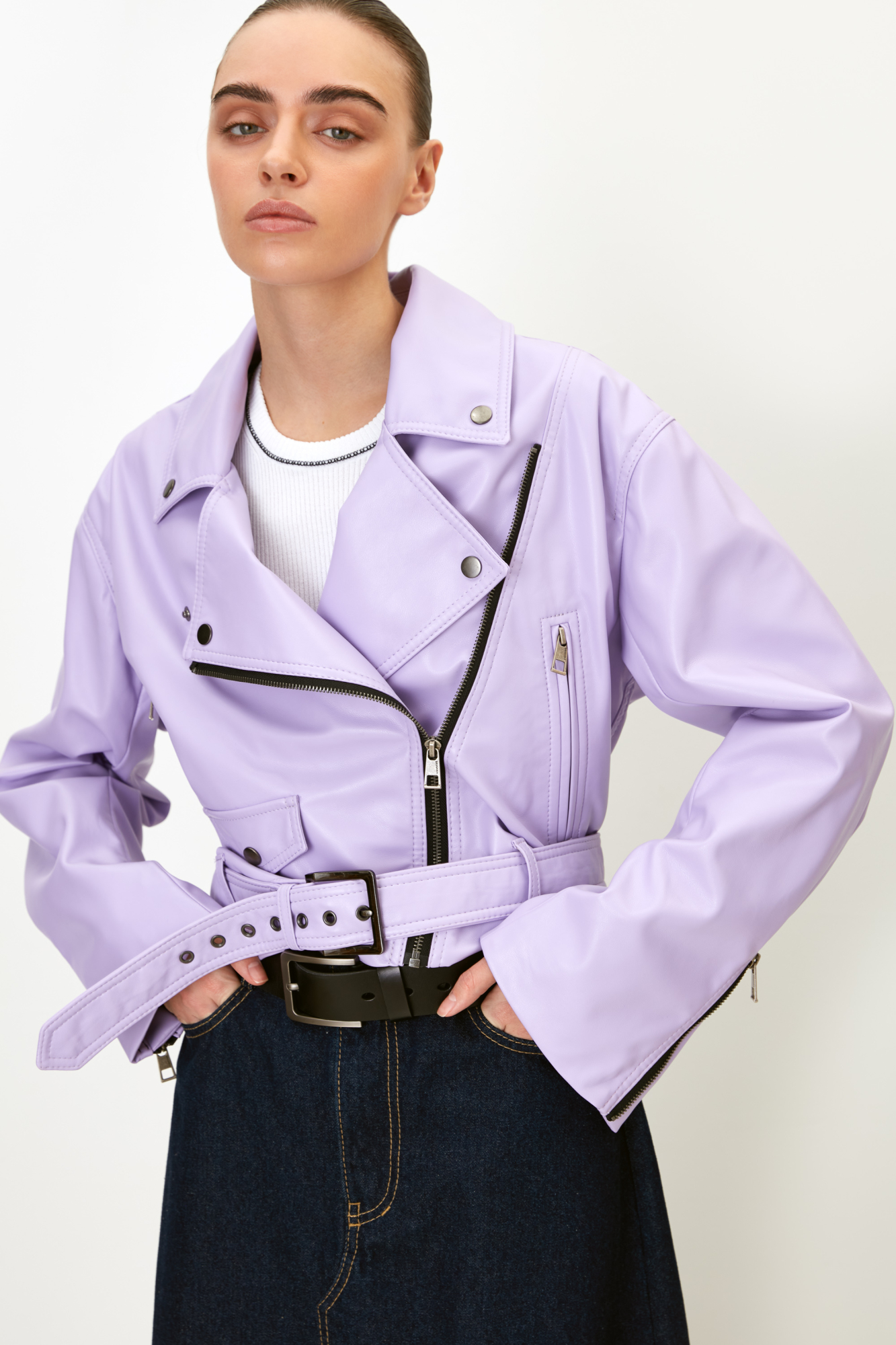 Короткая куртка-косуха из экокожи. Модель с отложным воротником, лацканами, боковыми карманами на молниях и накладным карманом на кнопке. Изделие дополнено шлевками на поясе и широким ремнем с люверсами и пряжкой. Застежка на молнию.