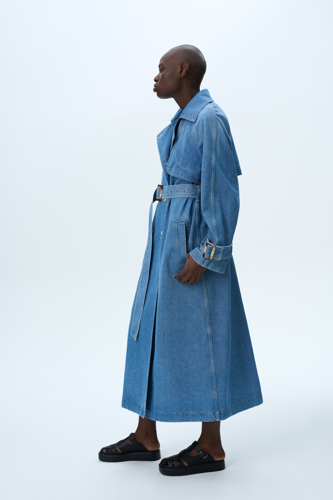 Двубортный джинсовый тренч на запах без подкладки. Асимметричная отлетная кокетка, отложной воротник, паты на манжетах и широкий пояс из основного материала.