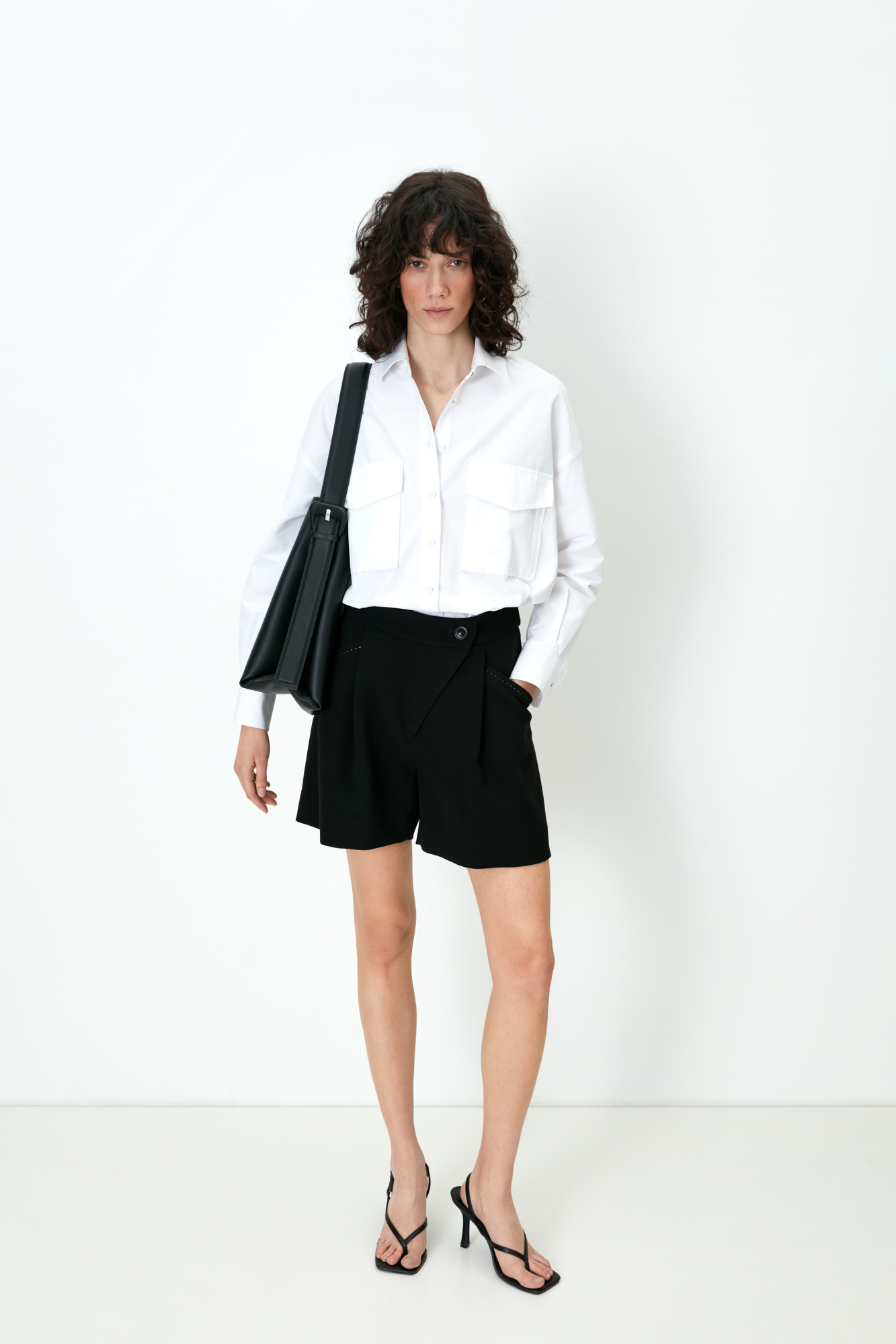 Шорты из поливискозы с косой застежкой и карманами по бокам. Дополнить образ можно рубашкой с накладными карманами и бежевым тренчем.