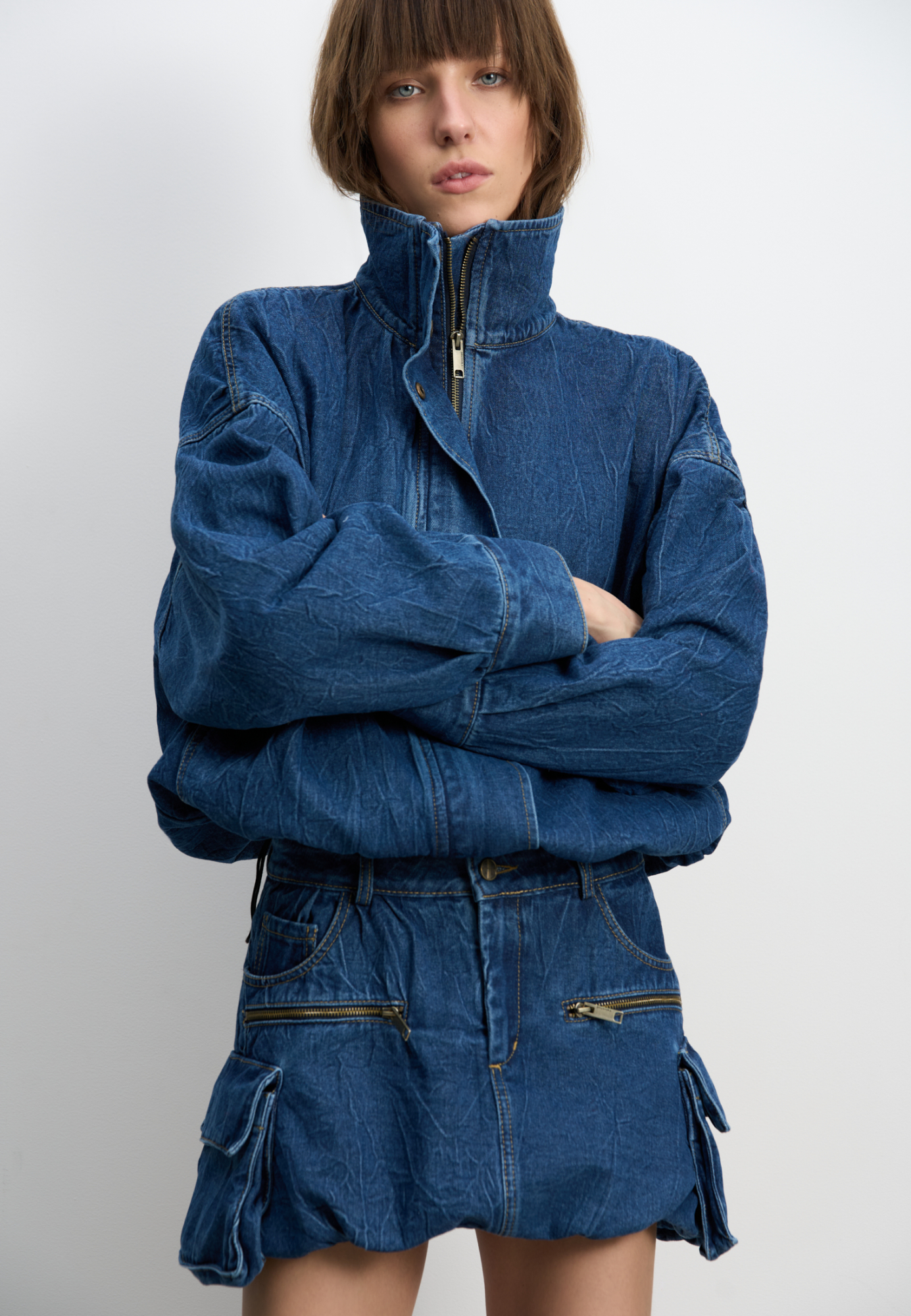 Джинсовая мини-юбка баллон из 100% хлопка. Модель с большими накладными карманами с клапанами по бокам, врезными карманами, шлевками на поясе для ремня и застежкой на молнию и пуговицу.