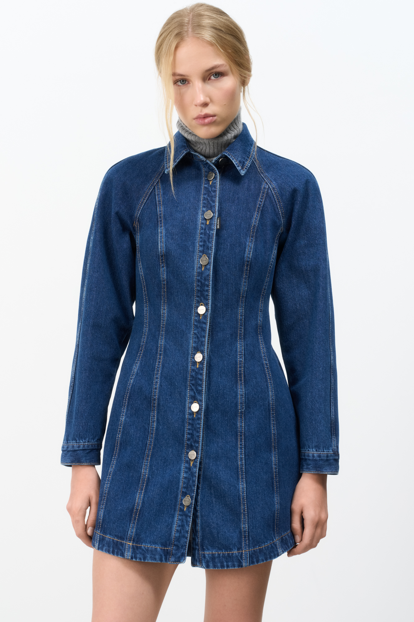 Джинсовое платье из 100% хлопка длины мини. Модель приталенного силуэта, с длинным рукавом реглан и отложным воротником. Застежка на пуговицы.