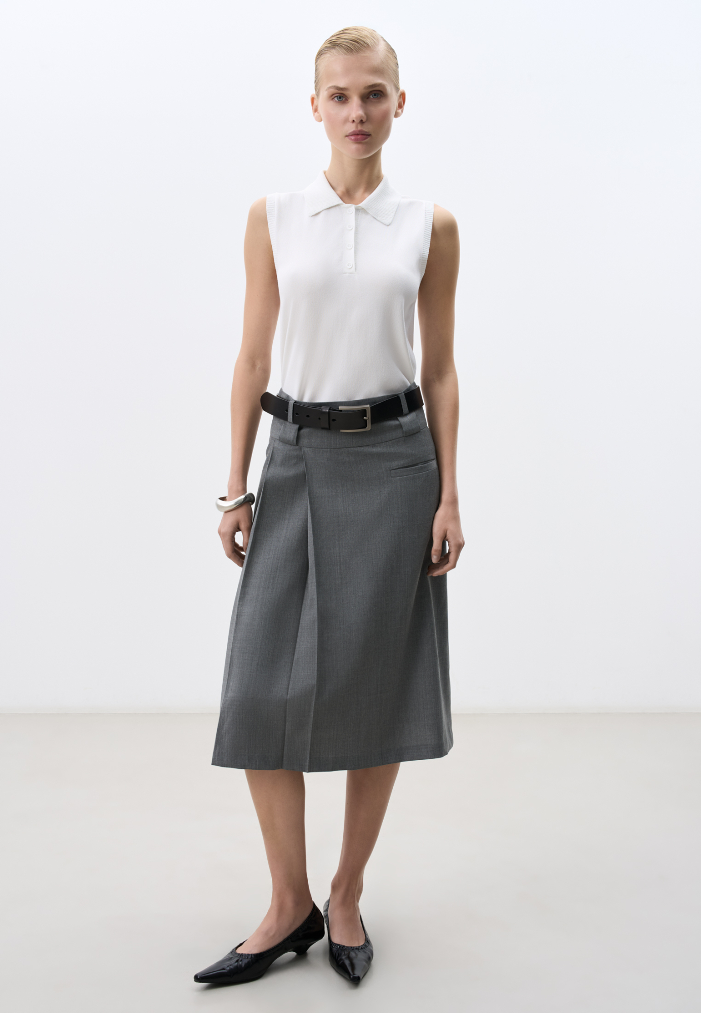 Юбка длины миди из шерсти. Модель прямого кроя, с двумя продольными складками сбоку, двойным поясом со шлевками для ремня, врезным карманом и застежкой на молнию. Изделие без подкладки.