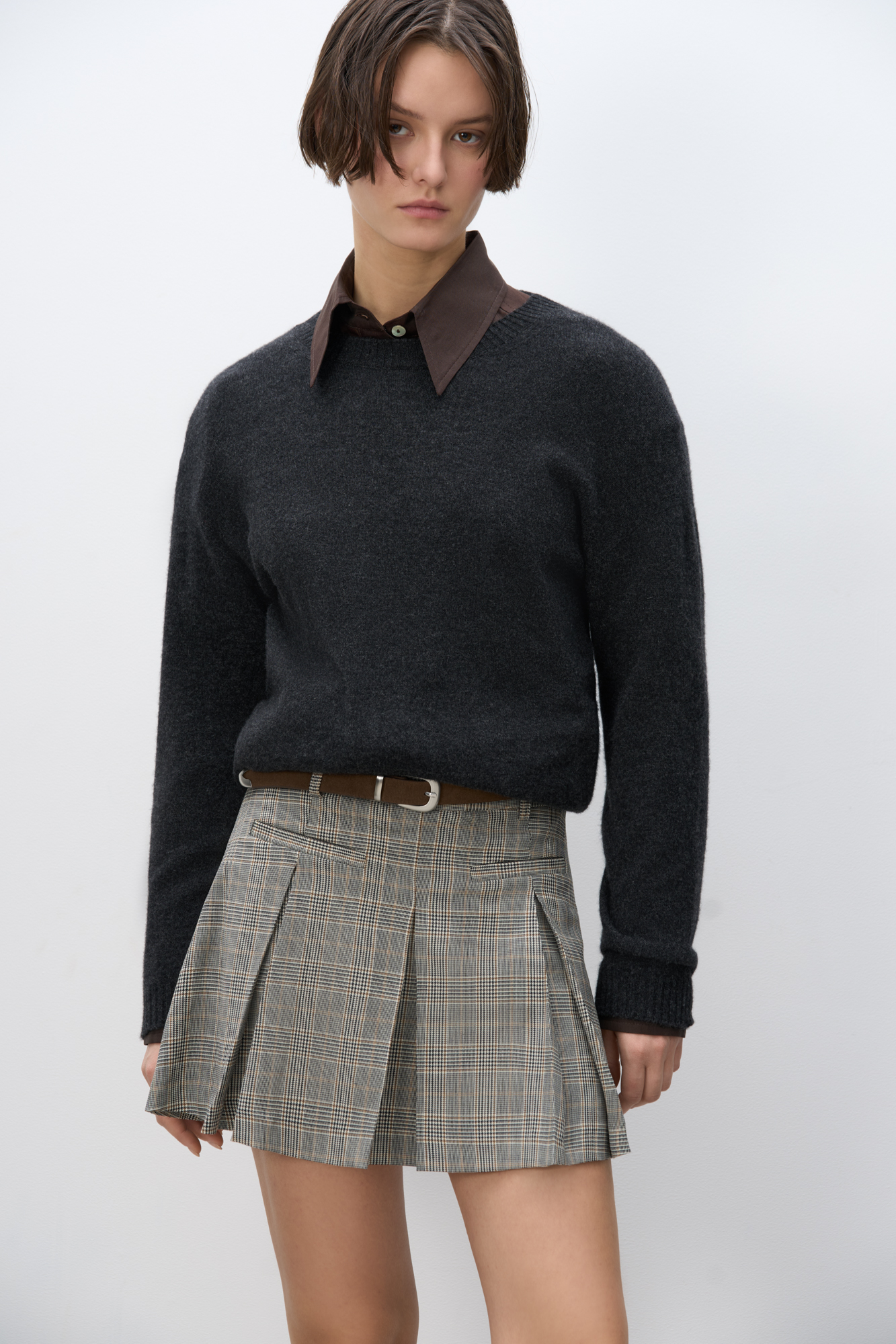 Юбка длины мини в клетку гленчек из шерсти. Модель прямого кроя, с крупными складками, поясом со шлевками для ремня, врезными карманами спереди и застежкой на молнию. Изделие без подкладки.