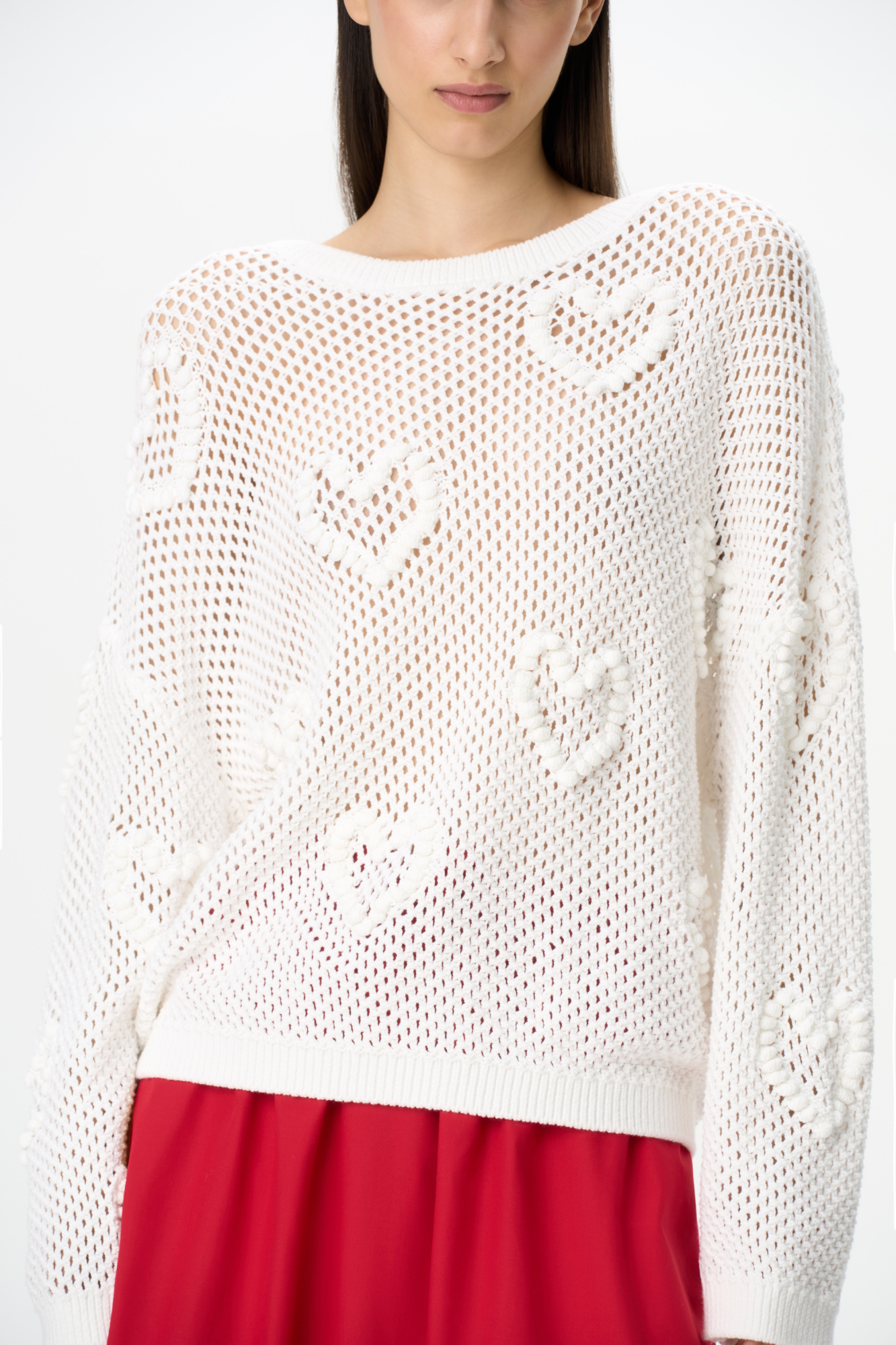 Трикотажный ажурный джемпер из хлопка. Модель свободного силуэта, со спущенной линией плеч, длинными рукавами и круглым вырезом горловины. Изделие декорировано объемными деталями в виде сердечек.