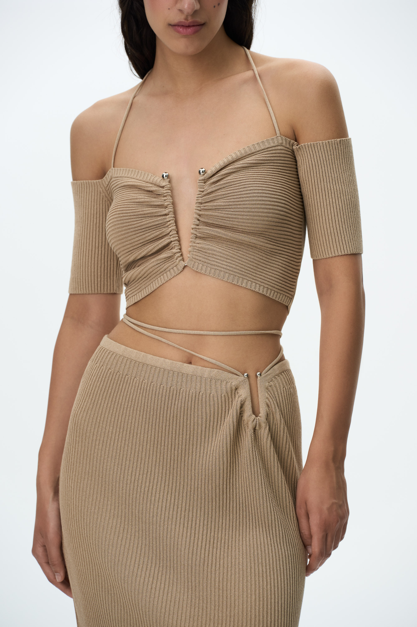 Трикотажный укороченный топ, декорированный металлической перемычкой на груди. Модель с открытыми плечами, короткими рукавами и тонкими бретелями, завязывающимися на шее.