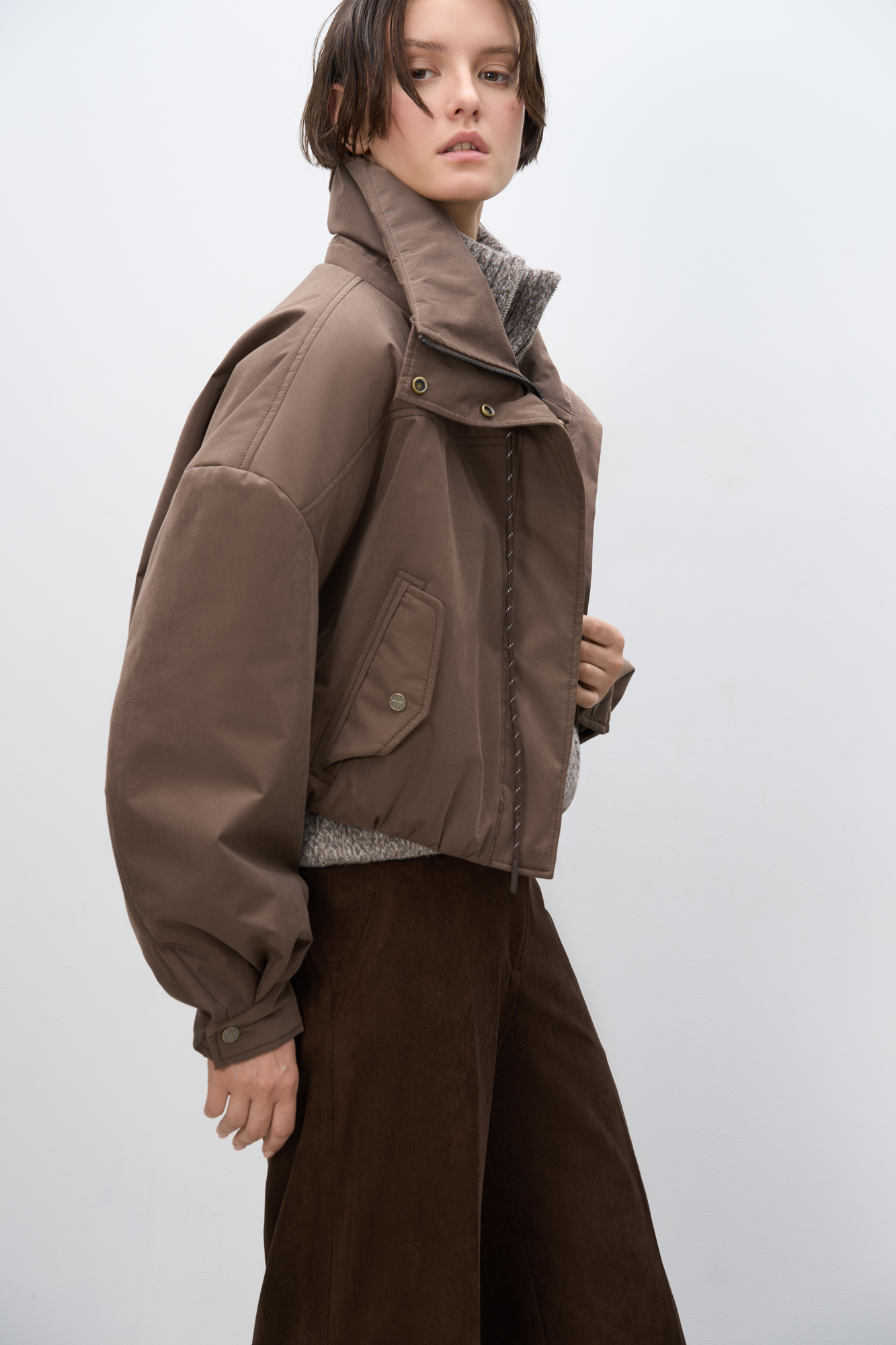 Объемный бомбер с воротником-стойкой. Модель укороченного силуэта со спущенной линией плеч, глубокими врезными карманами и застежкой на молнию под планку с кнопками. Манжеты рукавов декорированы металлическими брендированными кнопками.