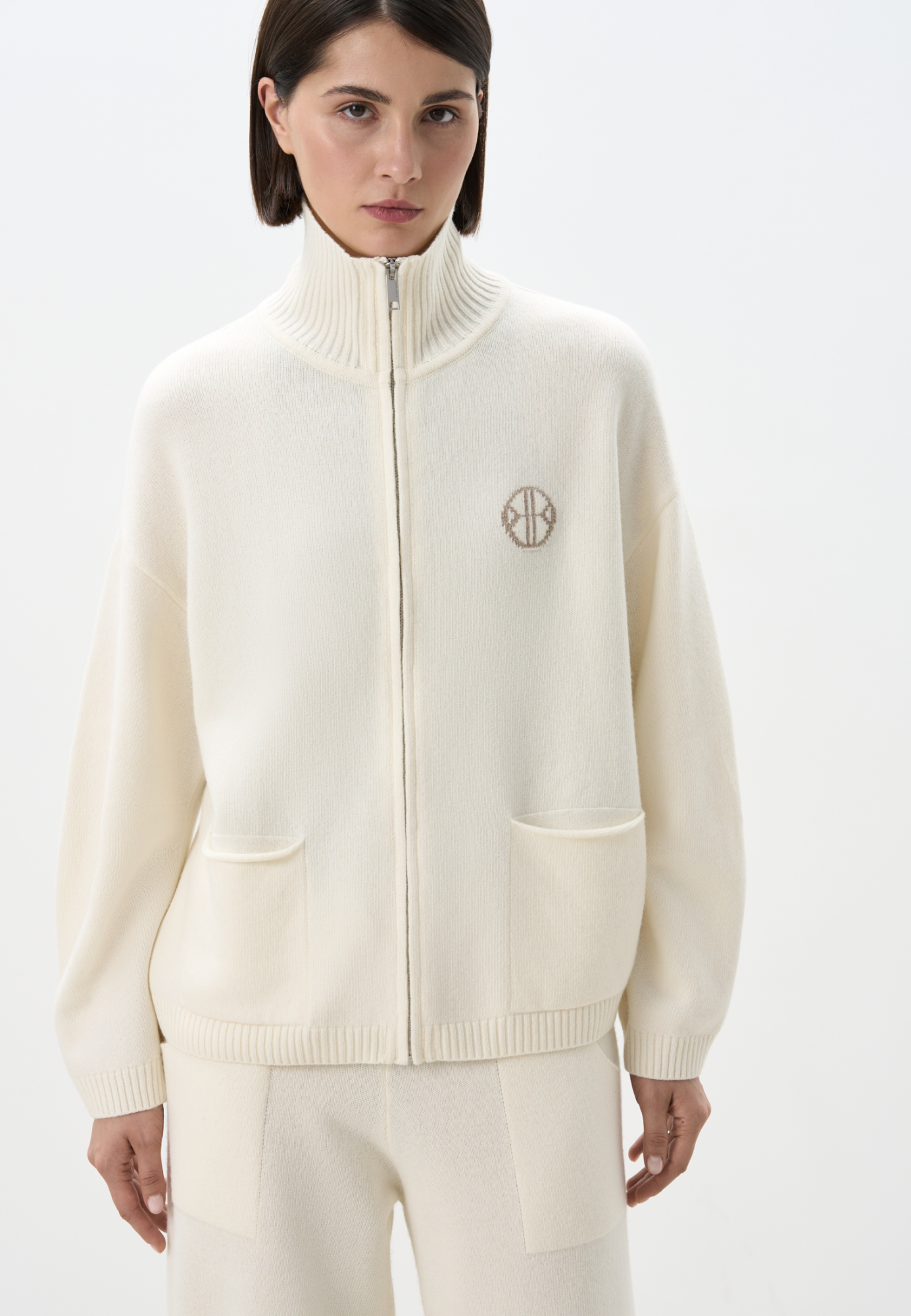 Трикотажный бомбер в спортивном стиле из кашемира и шерсти. Модель свободного силуэта со спущенной линией плеча, накладными карманами и воротником-стойкой. Изделие декорировано вышитым логотипом бренда на груди. Застежка на молнию.