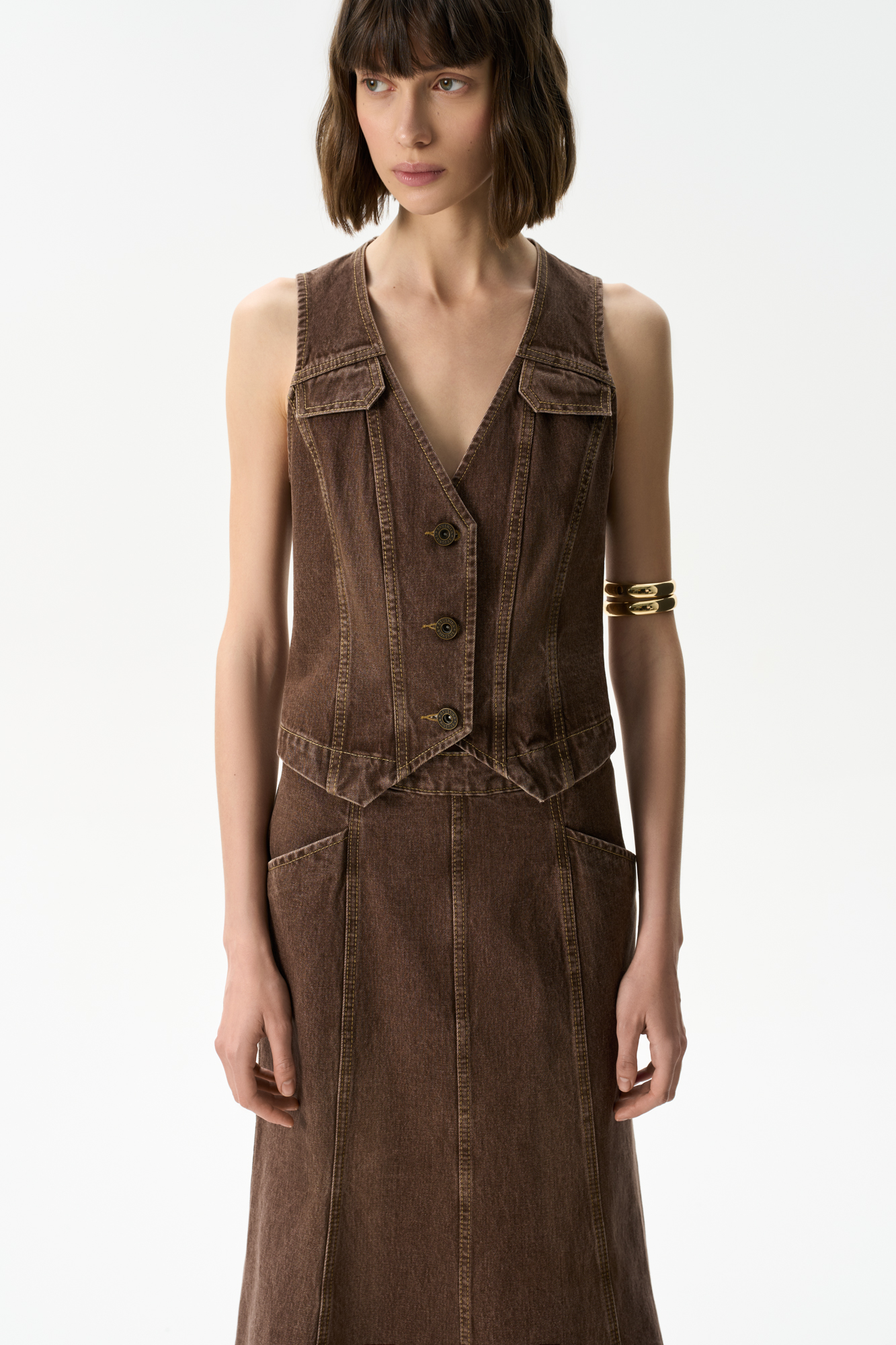 Джинсовый жилет из 100% хлопка. Модель прямого кроя с V-образным вырезом горловины и объемными вертикальными швами. Застежка на три металлические кнопки. Изделие без подкладки. 