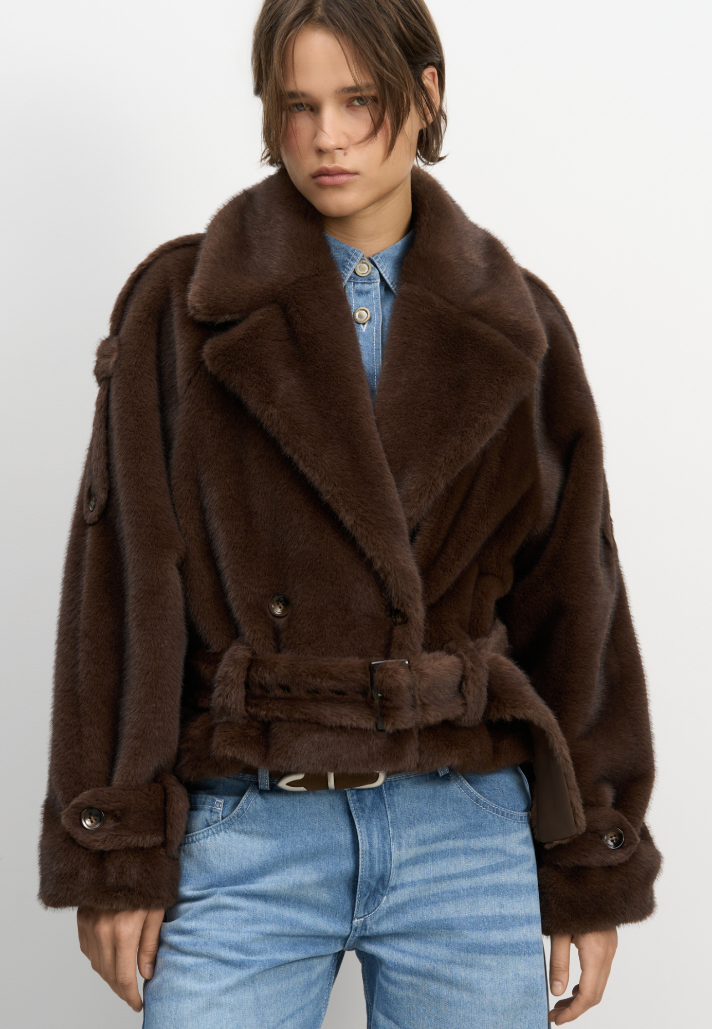 Короткая двубортная шуба из экомеха. Модель прямого кроя с широким отложным воротником. Изделие декорировано эполетами на плечах, широким поясом с пряжкой на талии и манжетах рукавов. Застежка на пуговицы. Изделие на подкладке.