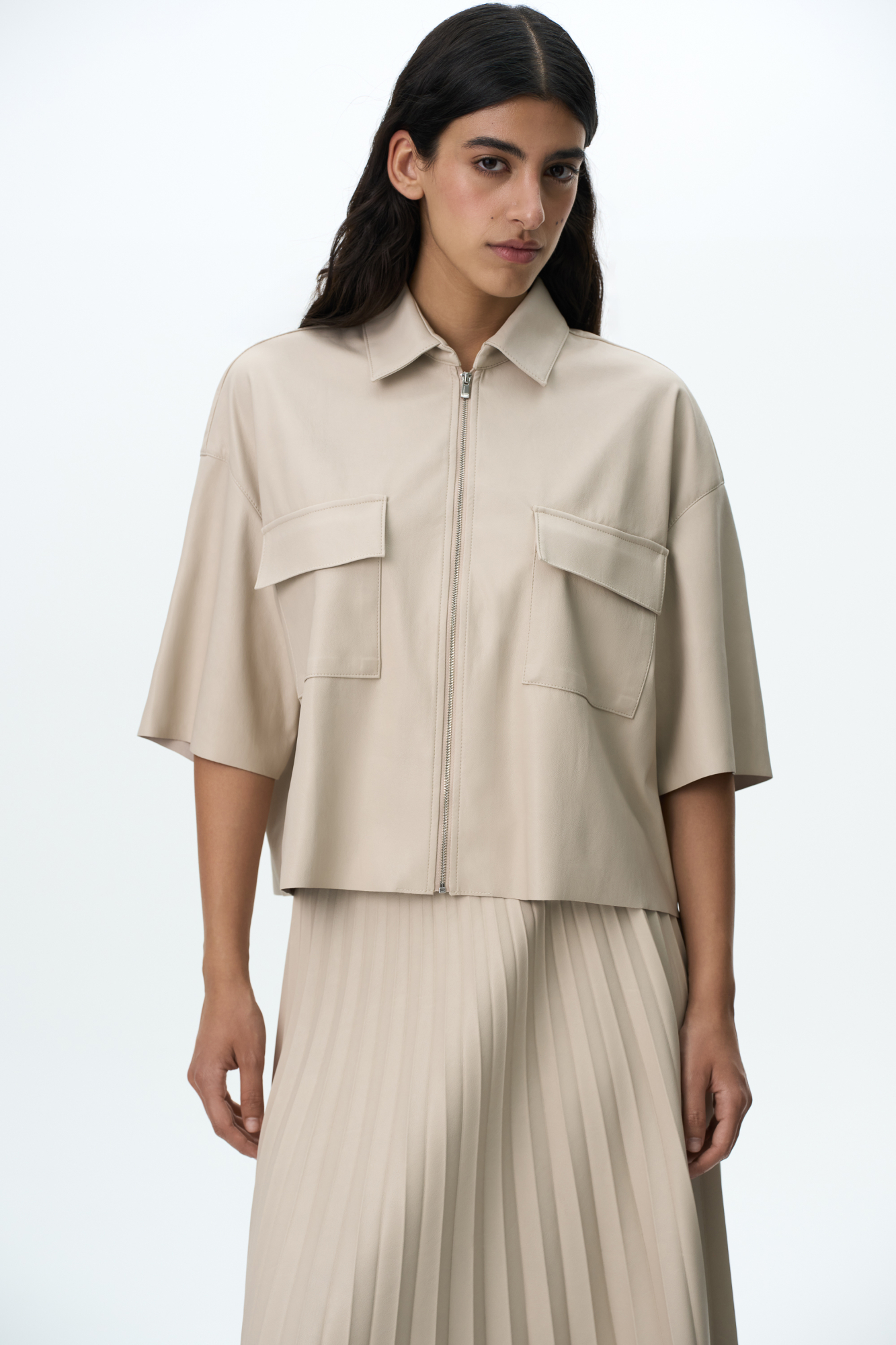 Укороченная рубашка из экокожи. Модель свободного силуэта со спущенной линией плеча, накладными карманами на груди и застежкой на молнию.