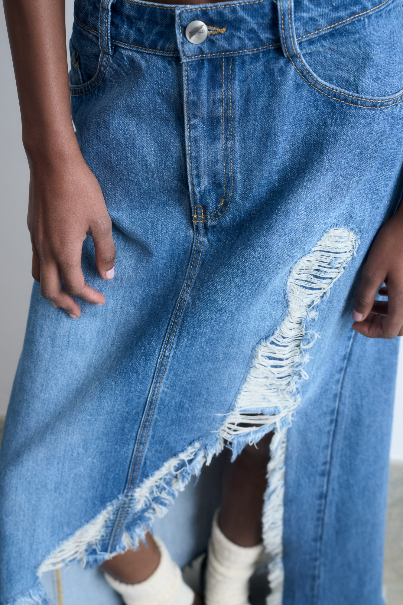 Джинсовая юбка из 100% хлопка в стиле гранж. Модель прямого кроя длины миди, со средней посадкой, пятью карманами и шлевками на поясе для ремня. Застежка на молнию и пуговицу. Изделие декорировано высоким рваным разрезом от бедра, создающим асимметрию юбки.