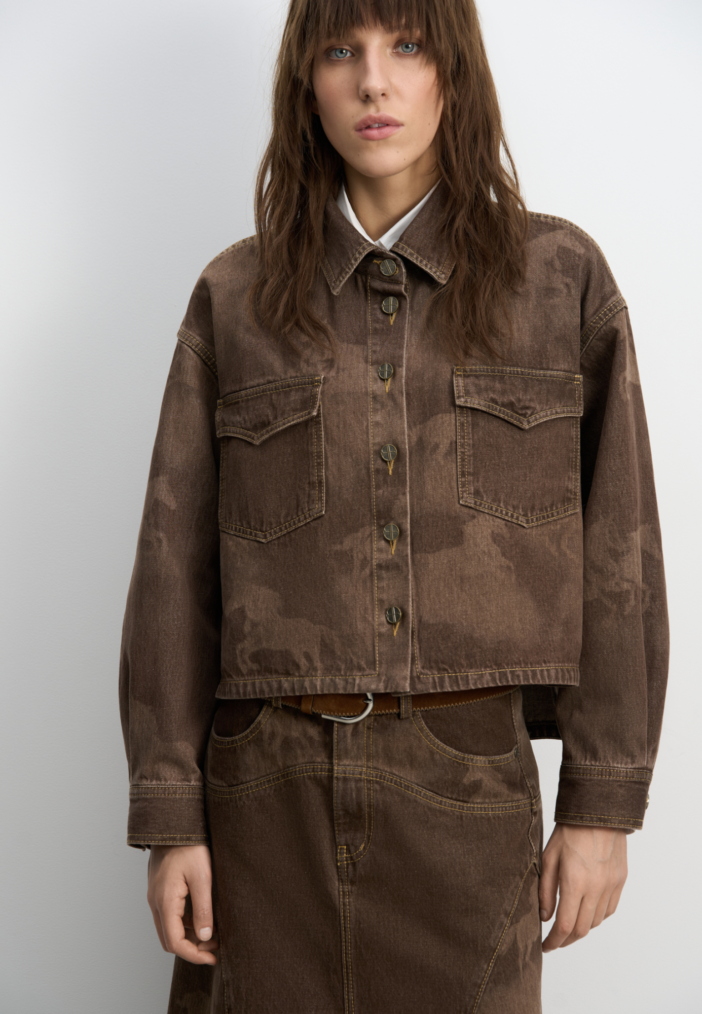 Джинсовая рубашка из 100% хлопка с принтом лошадей. Модель укороченного силуэта с длинными рукавами, классическим отложным воротником, нагрудными карманами с клапанами и застежкой на металлические пуговицы с логотипом бренда. Изделие декорировано принтом лошадей, выполненным лазером, и объемными геометрическими вытачками.<br />
Модель в стиле дерби - направления в моде, которое имитирует одежду для скачек.