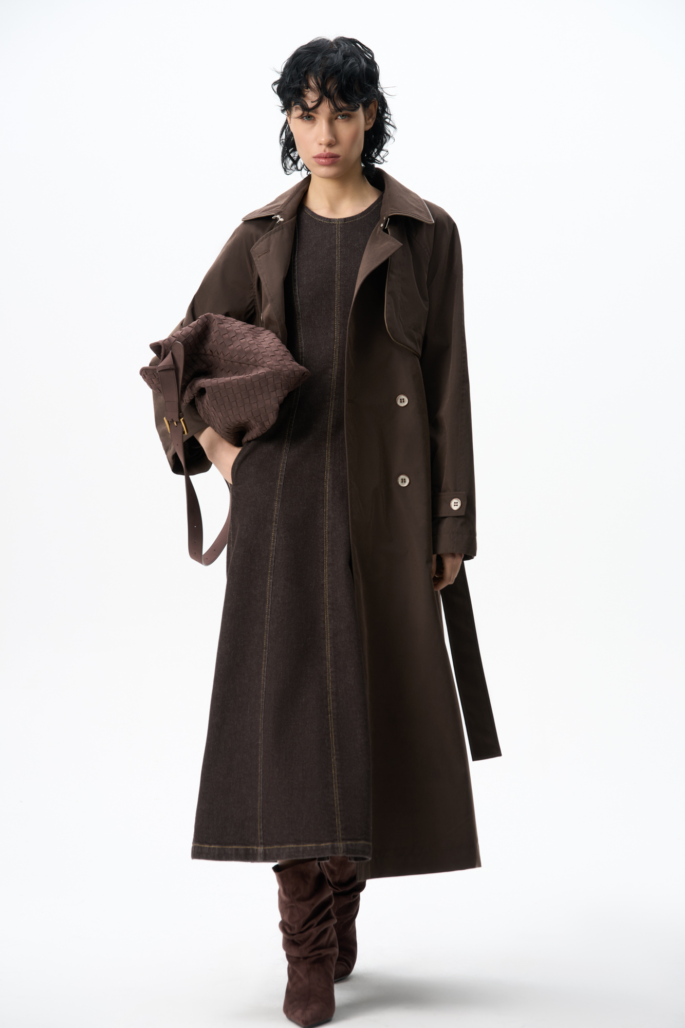 Двубортный длинный тренч прямого кроя. Модель с отложным воротником, декорированным металлической перемычкой, отлетной кокеткой, патами с пуговицами на манжетах, карманами и шлевками на талии для пояса.