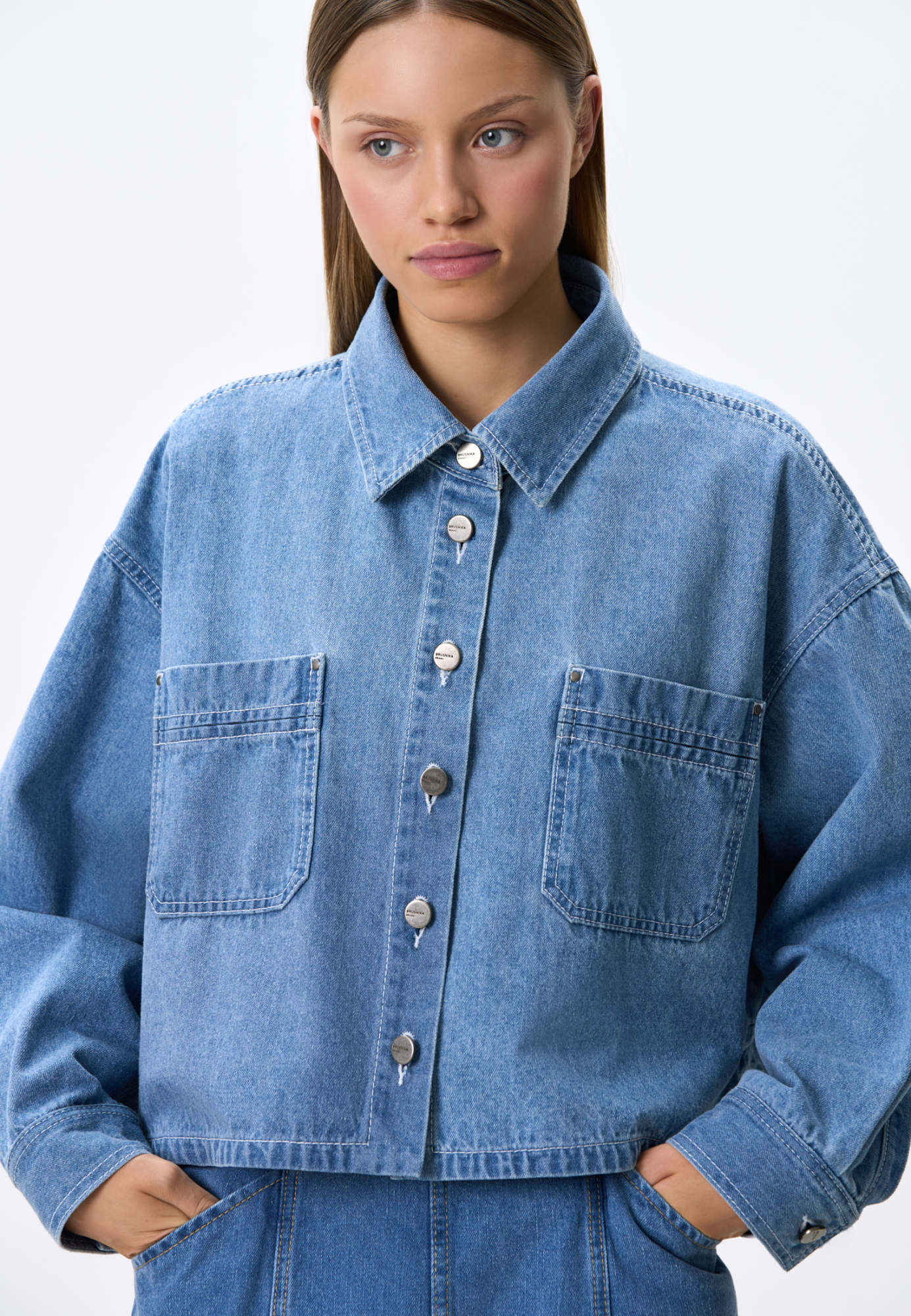 Укороченная джинсовая рубашка из 100% хлопка. Модель свободного силуэта, с отложным воротником, длинными рукавами и нагрудными карманами. Застежка на пуговицы.