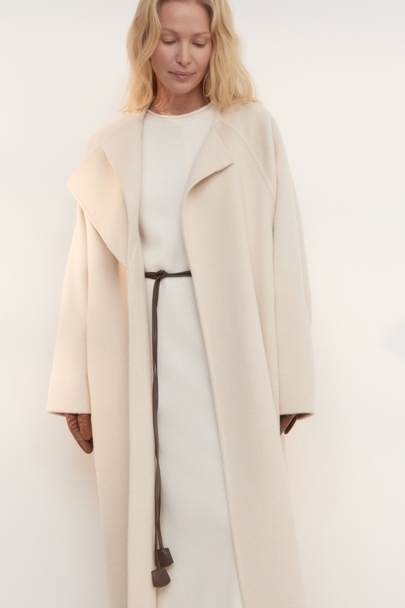 Шерстяное пальто из двусторонней ткани. Модель прямого кроя без воротника. Застежка на скрытые магнитные пуговицы. Изделие без подкладки. Модель декорирована асимметричным лацканом. Пояс из экокожи в комплекте.