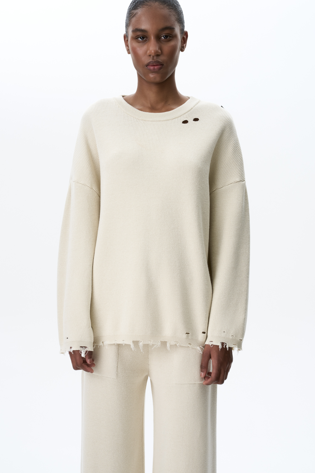 Трикотажный джемпер из хлопка с добавлением вискоза. Модель свободного силуэта со спущенной линией плеча и круглым вырезом горловины. Изделие декорировано имитацией драни и необработанным краем.