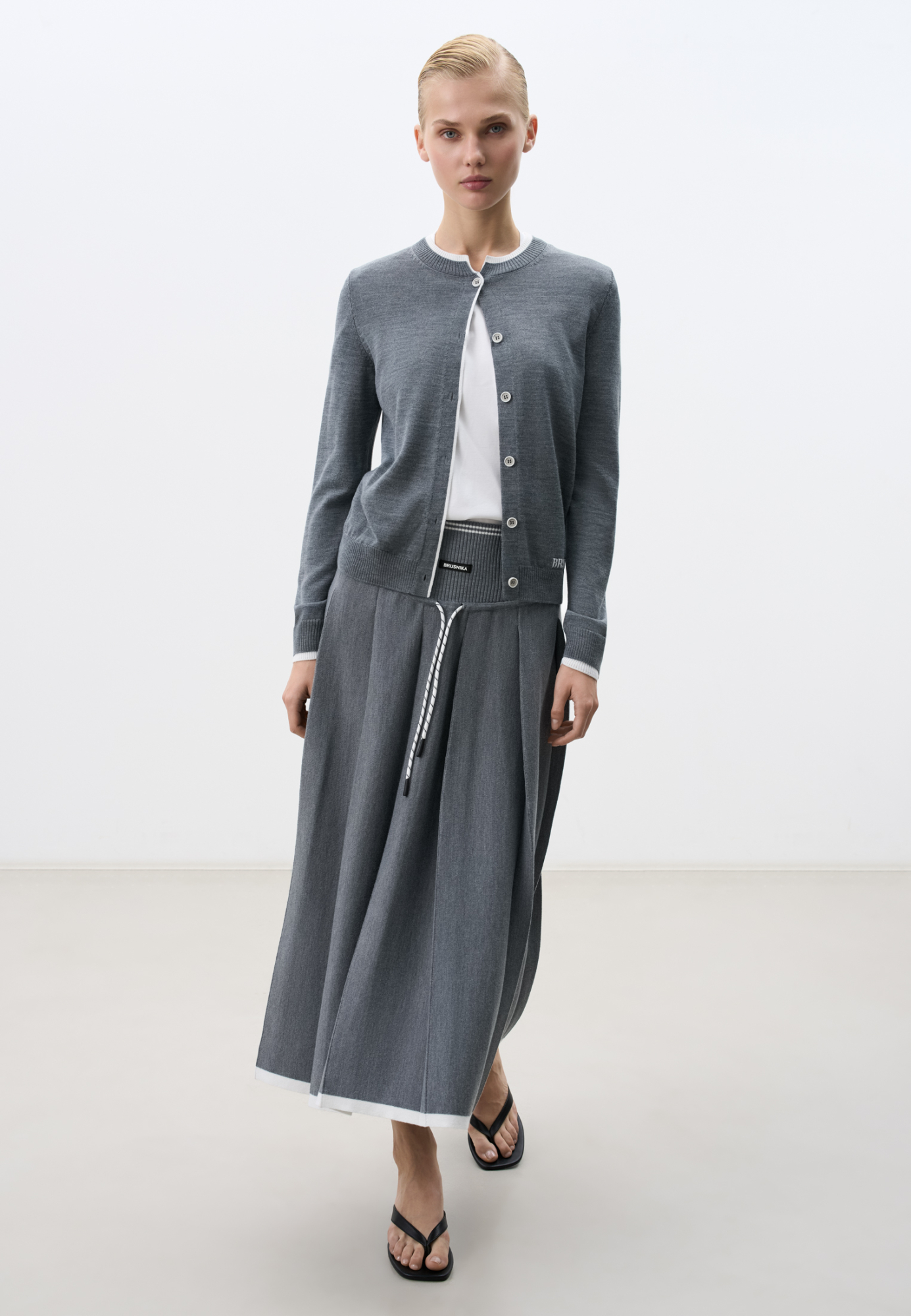 Трикотажная юбка плиссе длины миди из шерсти. Модель А-силуэта с широкими складками на кокетке дополненной шнурком. Кокетка выполнена в рубчик и декорирована лампасом контрастного цвета и брендированным ярлыком спереди.